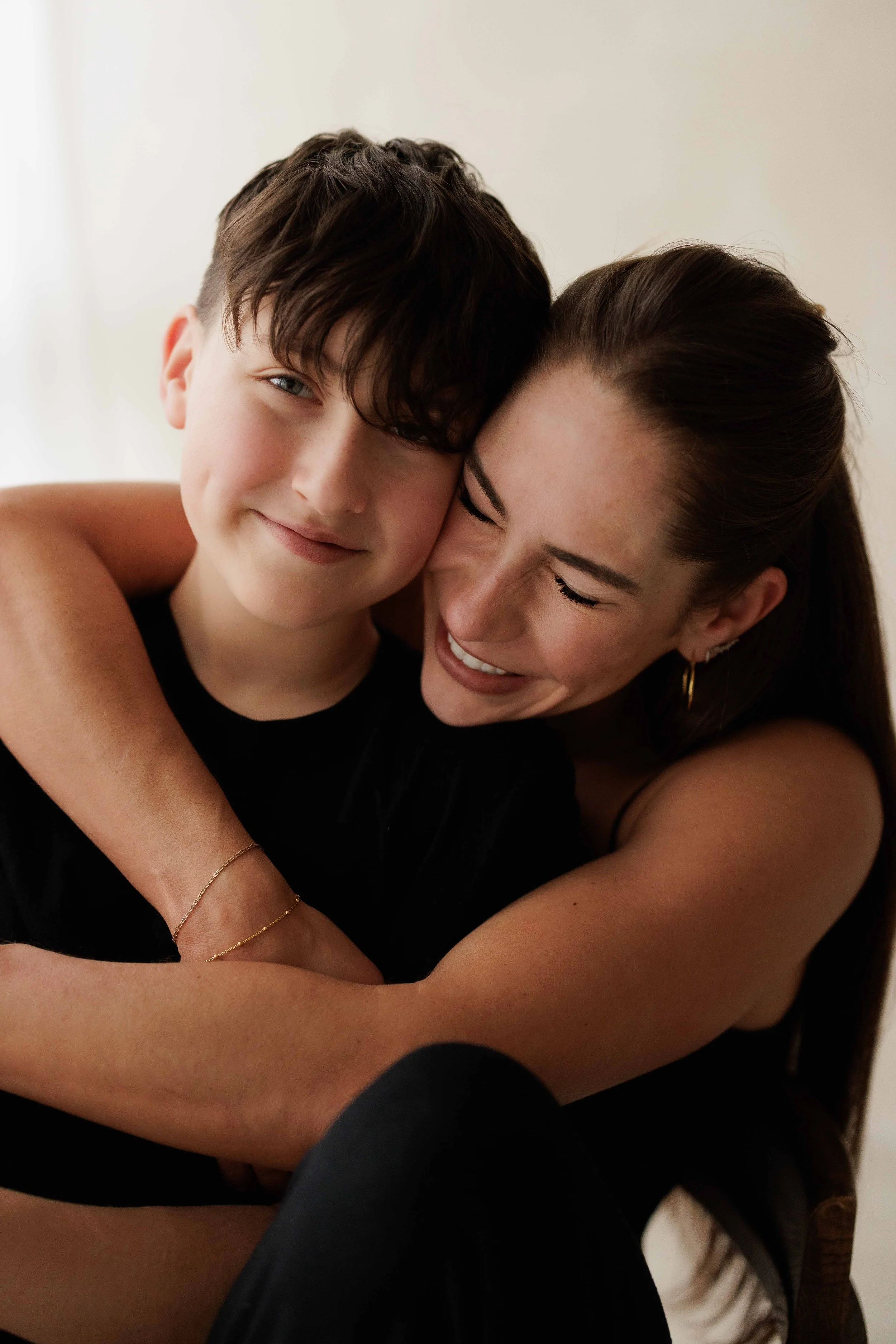 A mum and a young boy hugging and smiling in a close-up portrait.