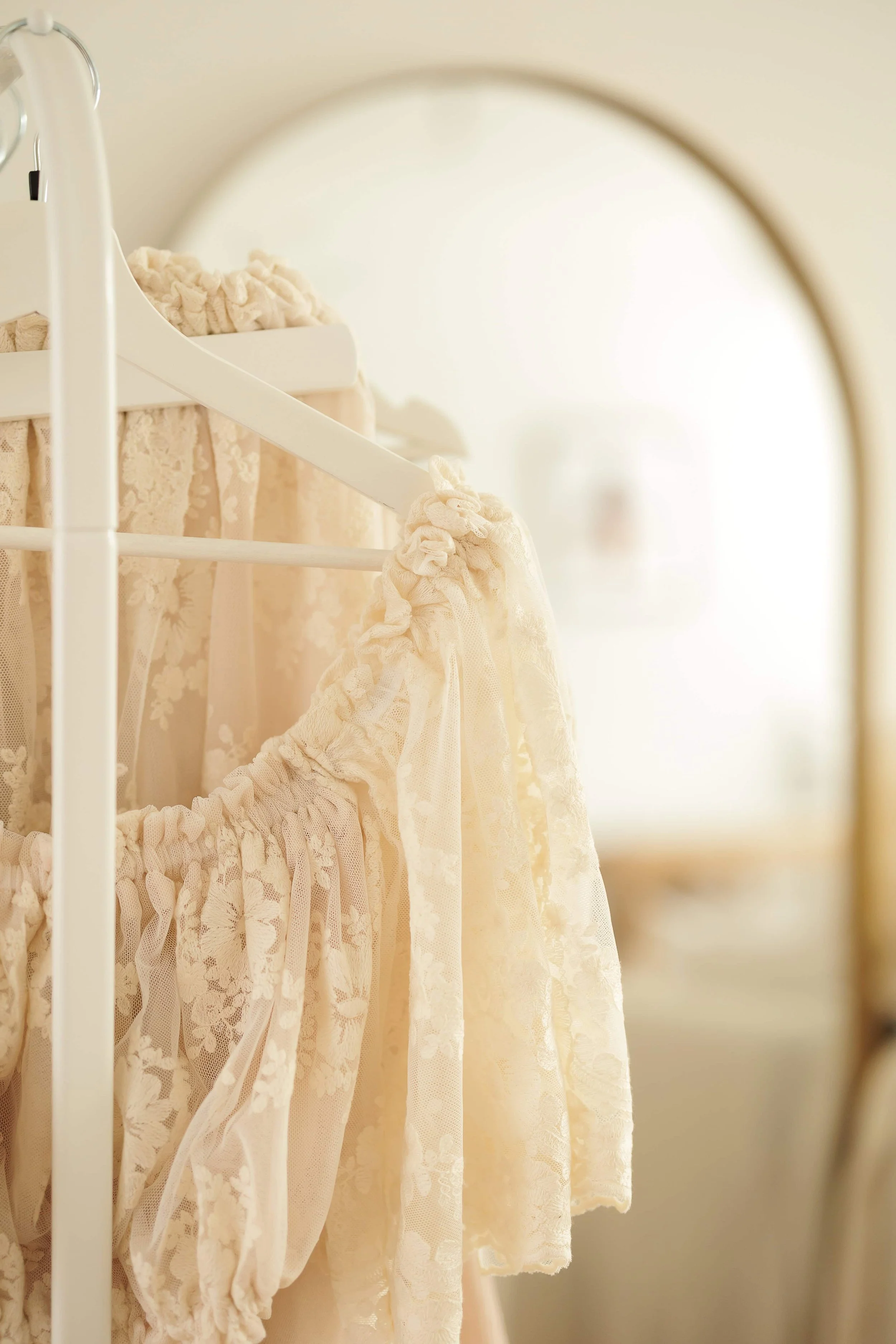 Lingerie and lace clothing hanging on a white clothing rack, reflected in a mirror.