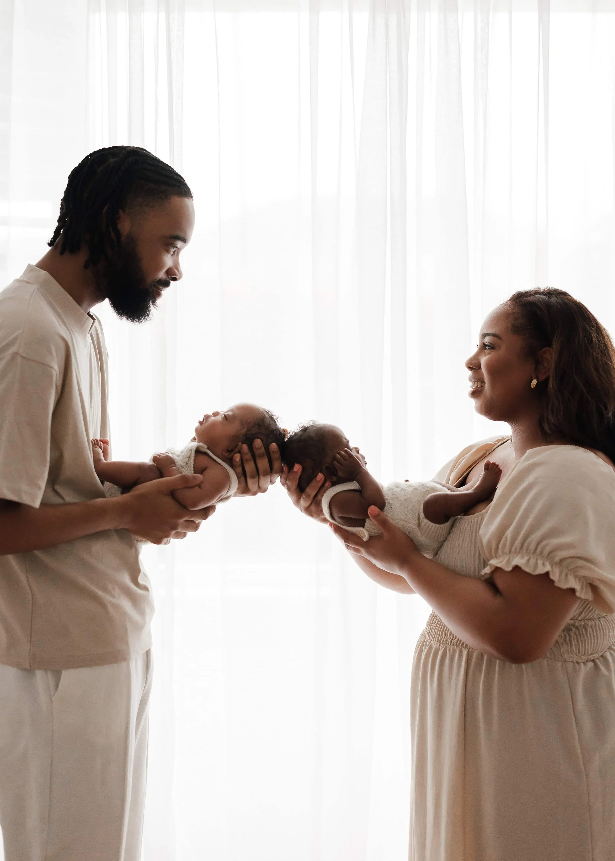 mum and dad holding their newborn twins in their arms in front of a window during a photoshoot in a studio in London