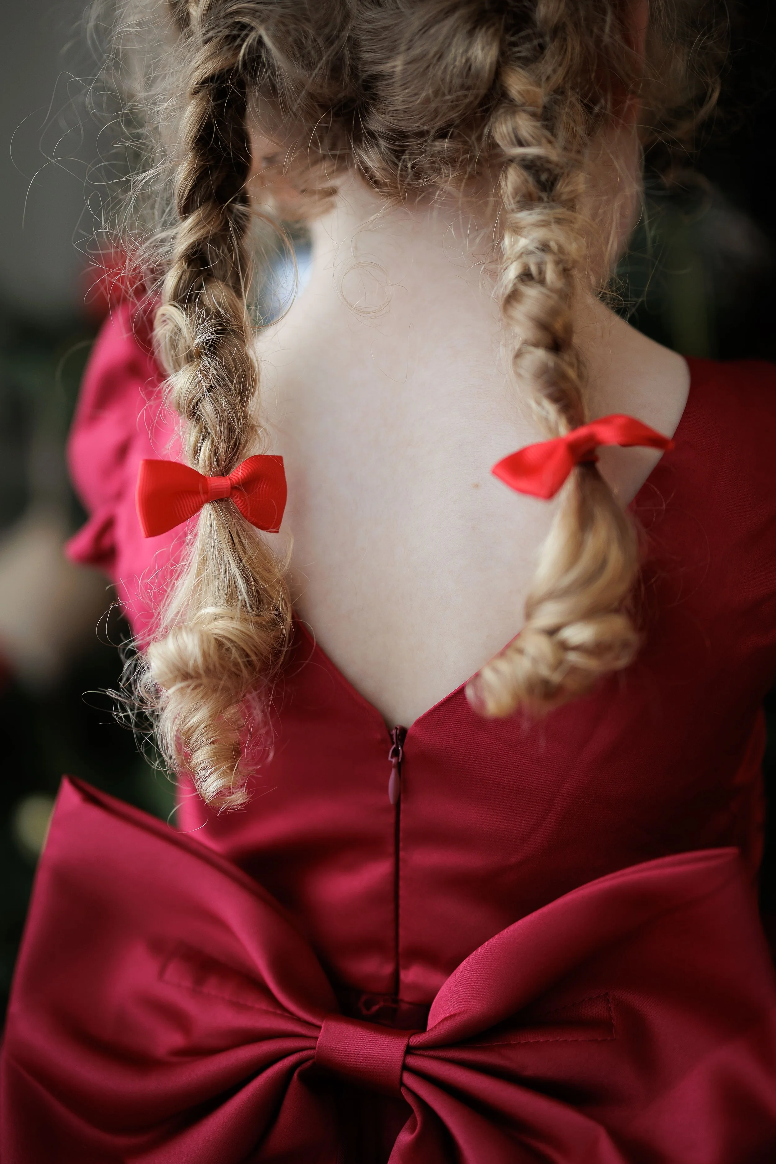 Close-up of a girl in a red dress with bows in her braided hair and a large bow at the waist.