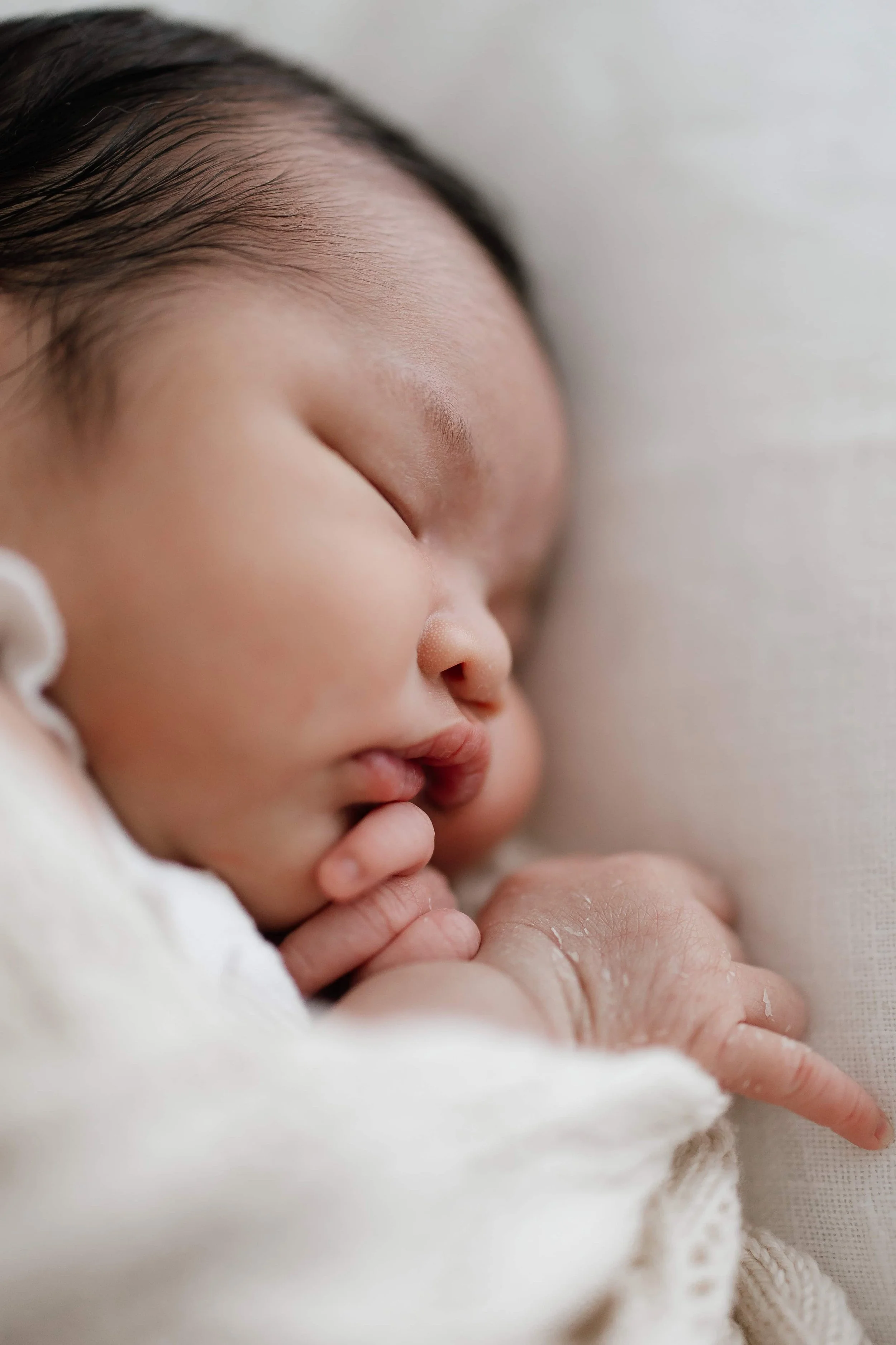 Close-up of a sleeping newborn baby with closed eyes and hand near face.