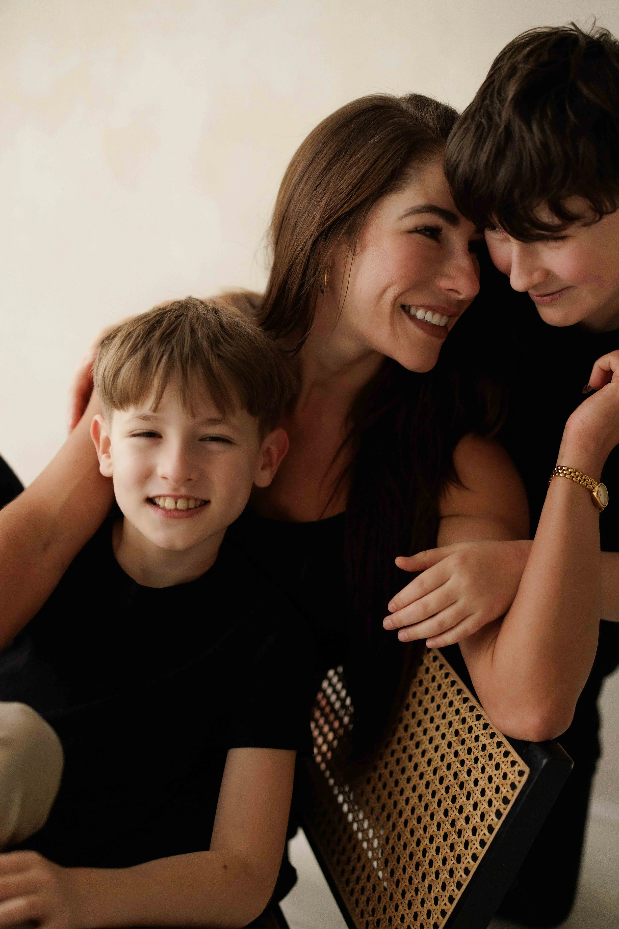 A mum, a teenage boy, and a young boy smiling and cuddling together during their family photoshoot in London