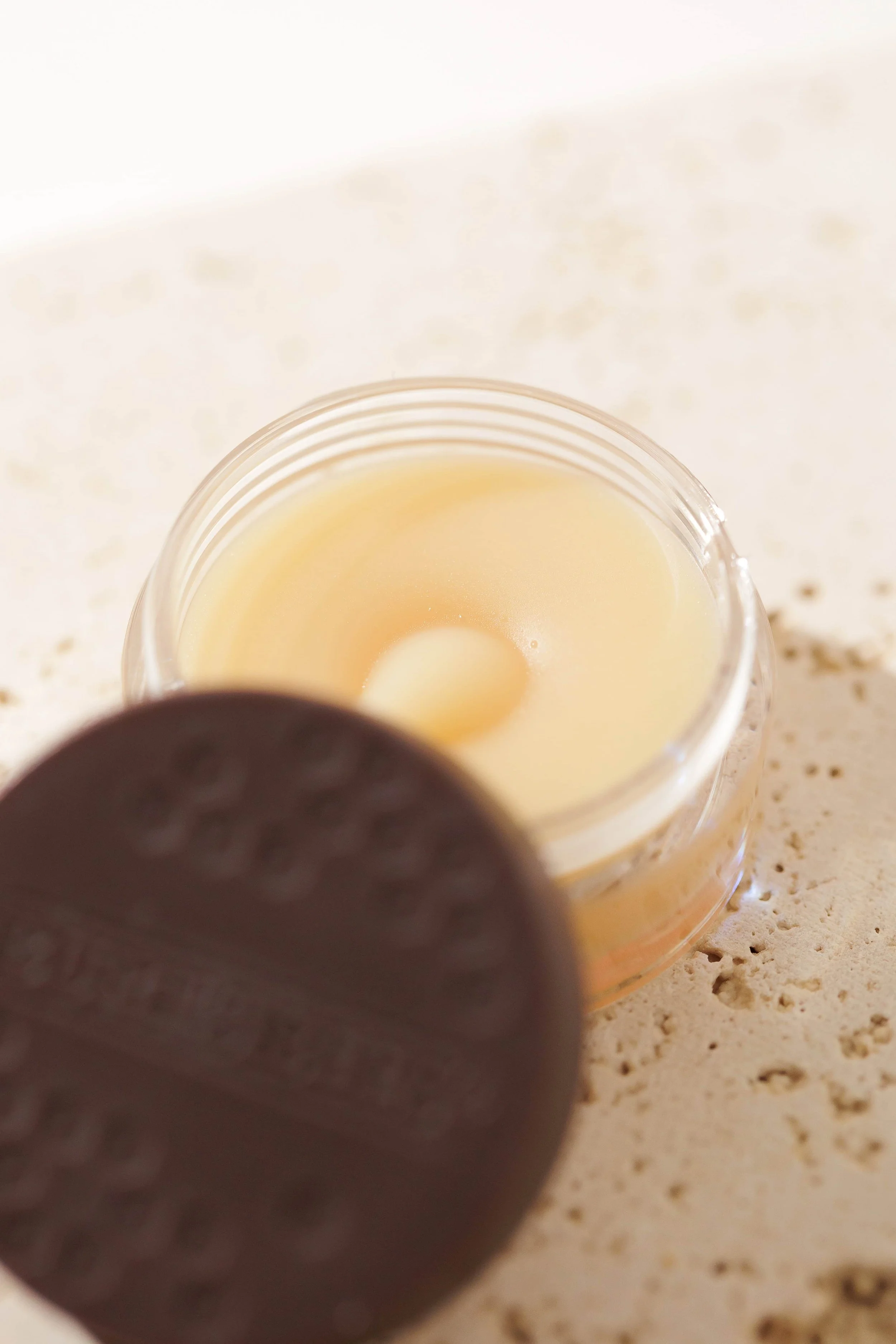 Close-up of an open jar of Vaseline with a partially peeled label on a sandy surface.