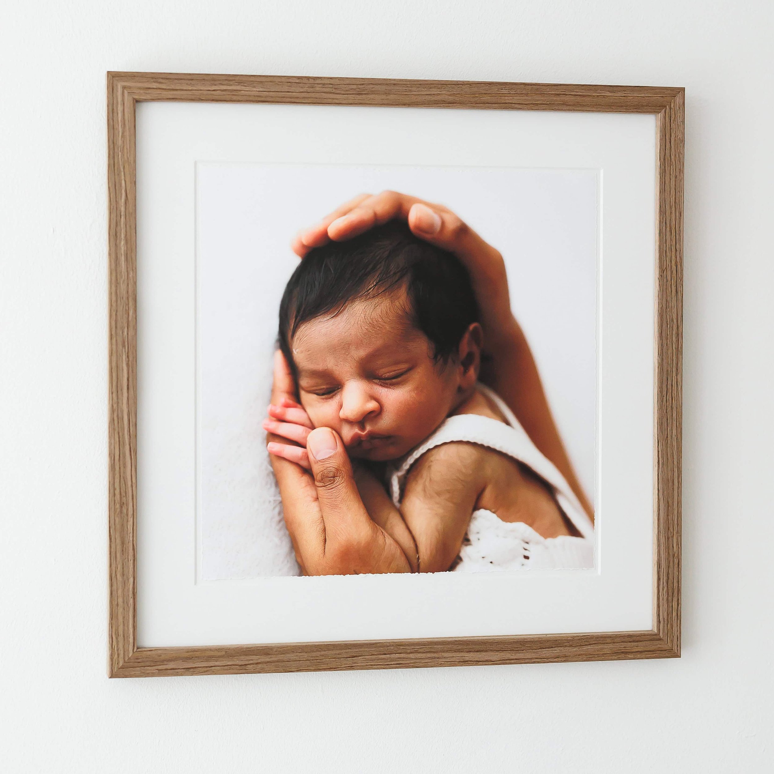 Framed photo of a newborn baby cradled by adult hands against a white background.