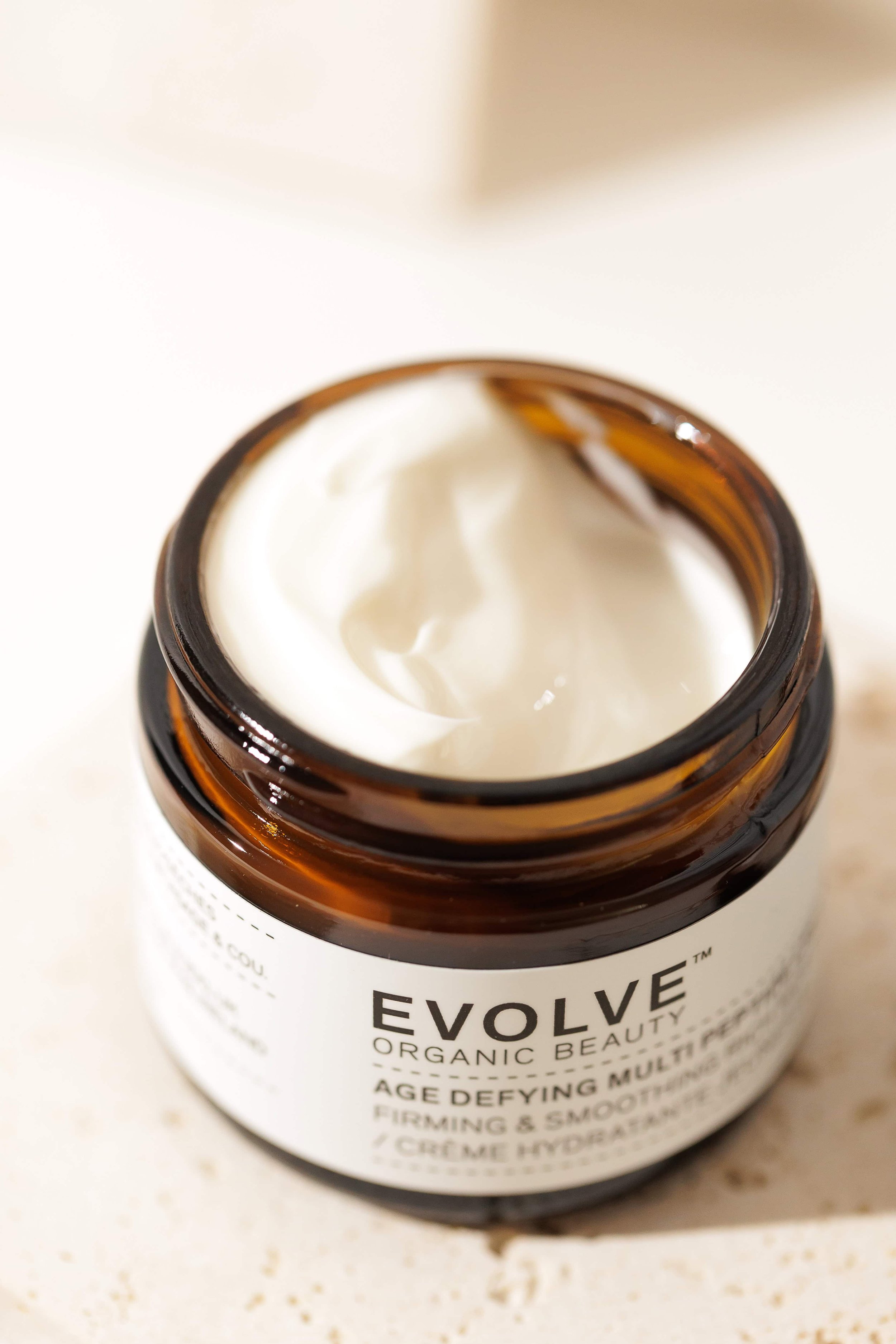Open jar of EVOLVE Organic Beauty age defying multi-cream on a light-colored surface.