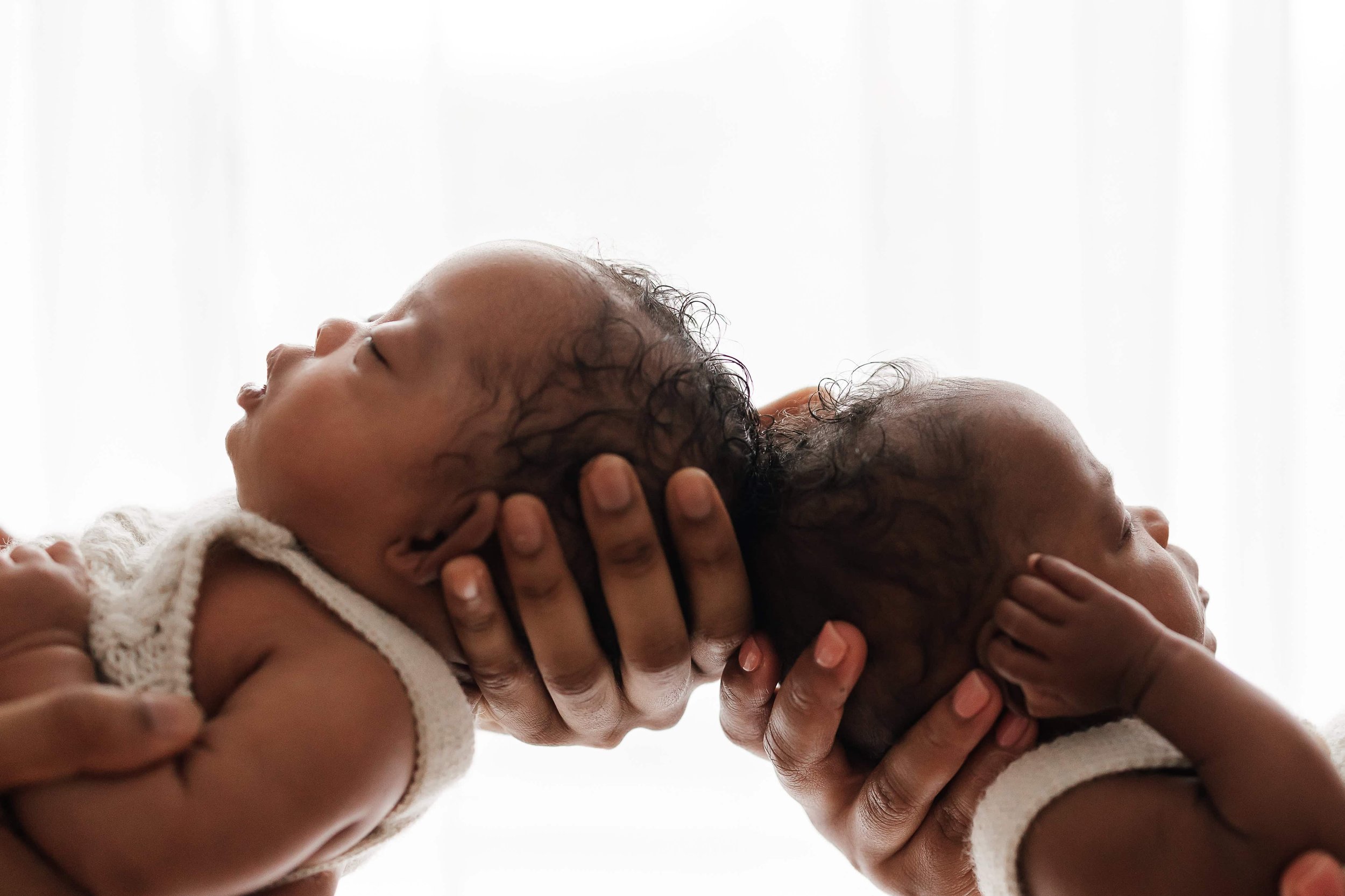 newborn twins being held by their parents and touching their heads
