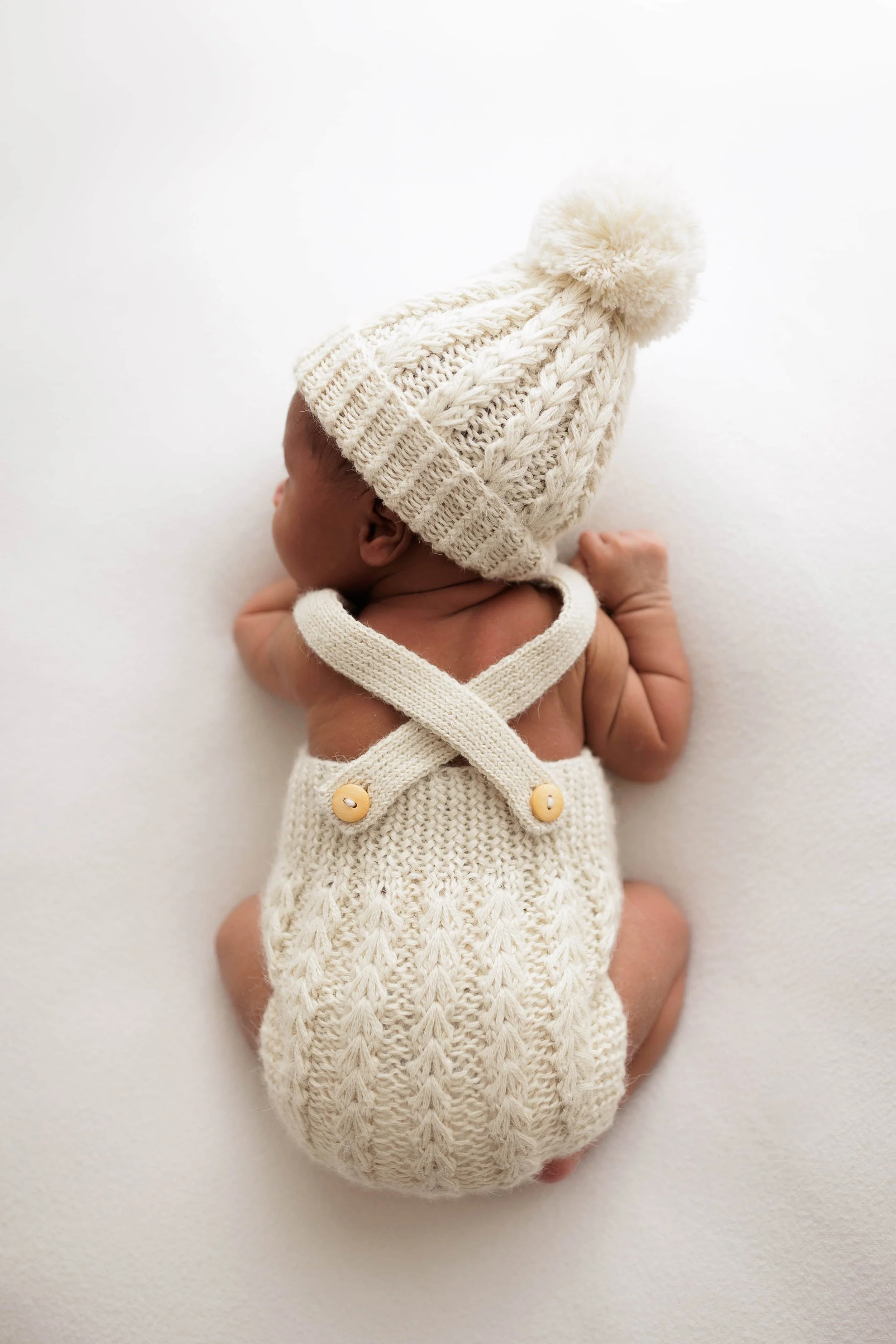 newborn baby sleeping on her tummy and wearing a beautiful knitted beige romper with a beanie hat from hank knitwear brand