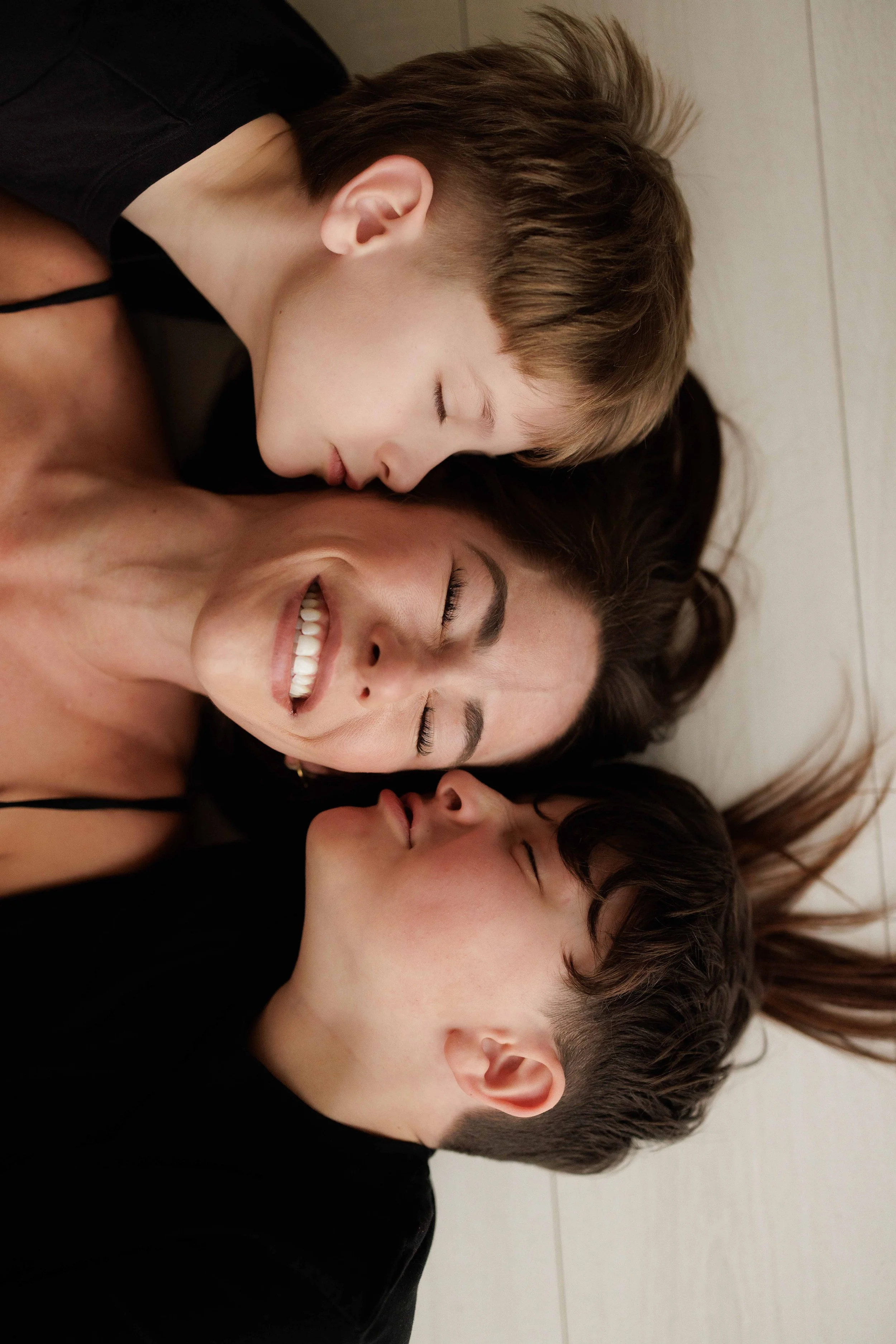A mum and her 2 boys lying on the floor with their heads close together, smiling and enjoying each other's company.