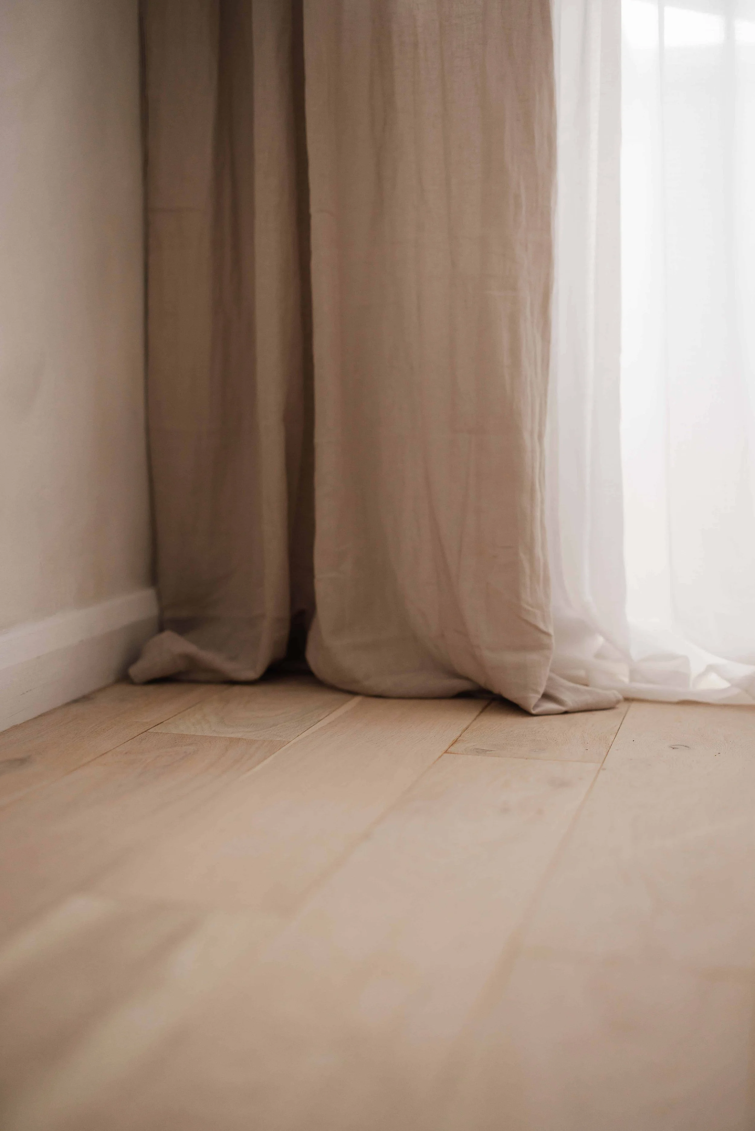 Close-up of beige curtains and light-colored wooden floor near a window with sheer white curtains, in a photography studio in Warlingham