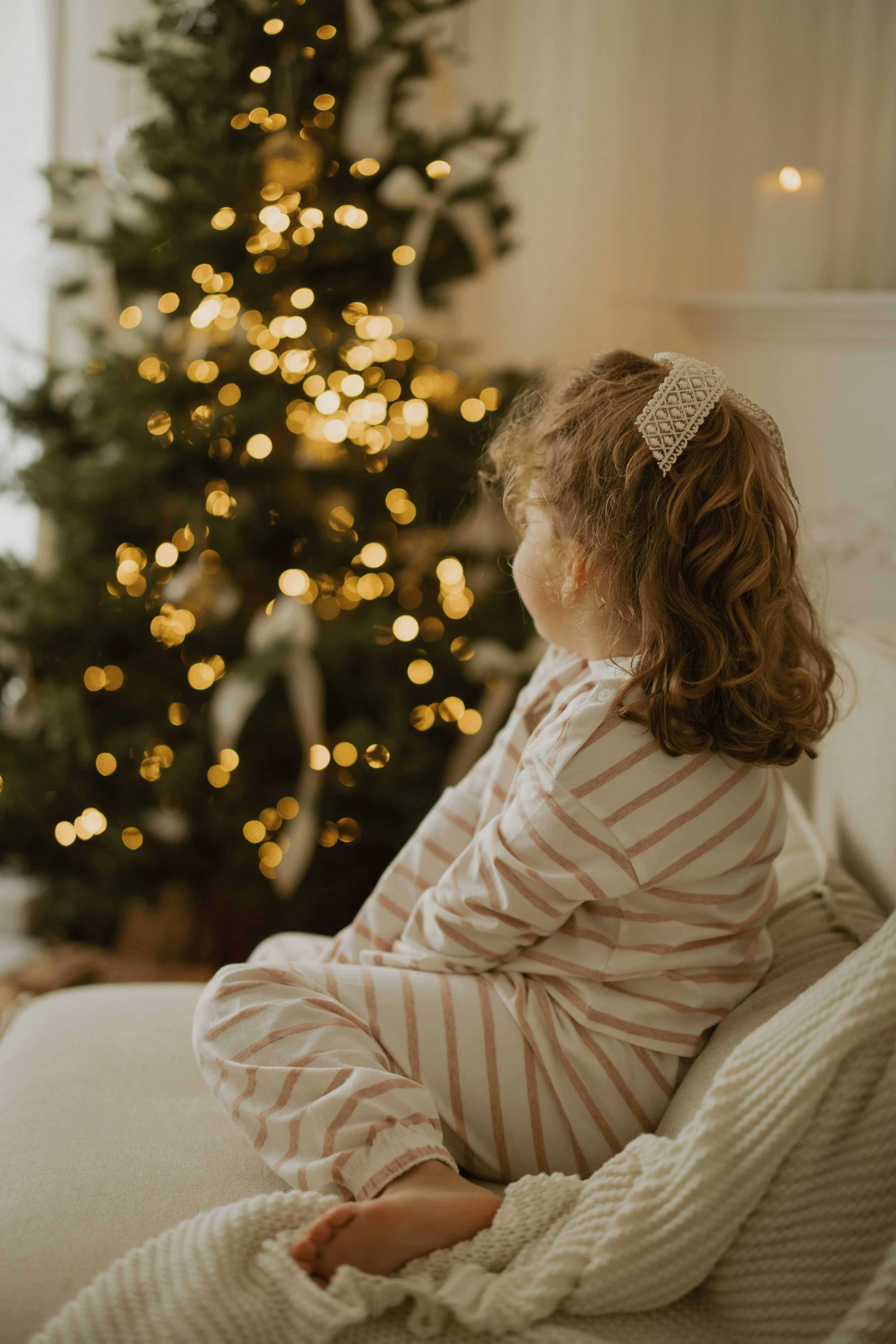 little girl searing a pyjama from the white company, seated on a sofa and looking at a christmas tree in a warm decor in a studio in Warlingham Surrey