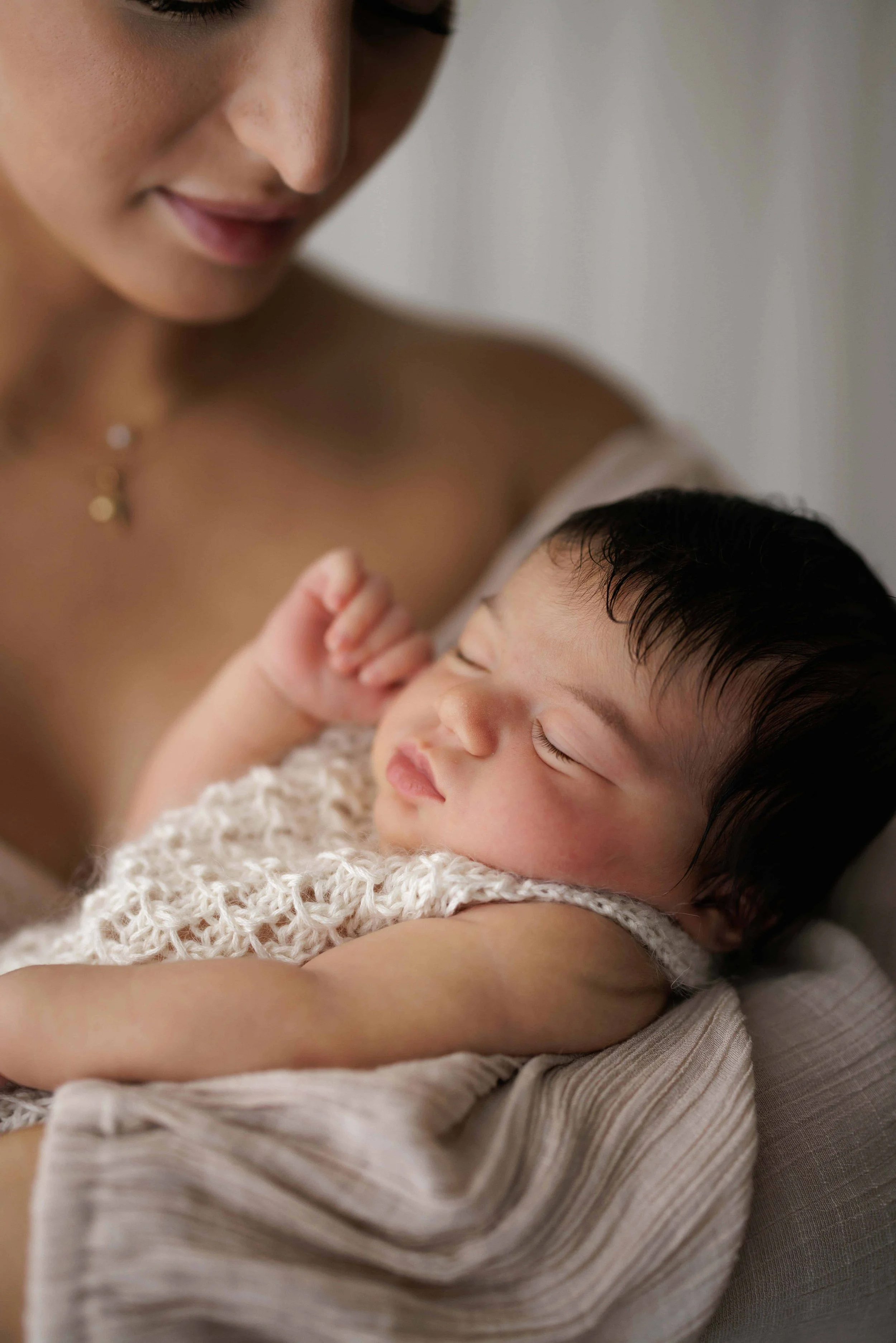 A woman holding a sleeping baby wrapped in a knitted blanket.