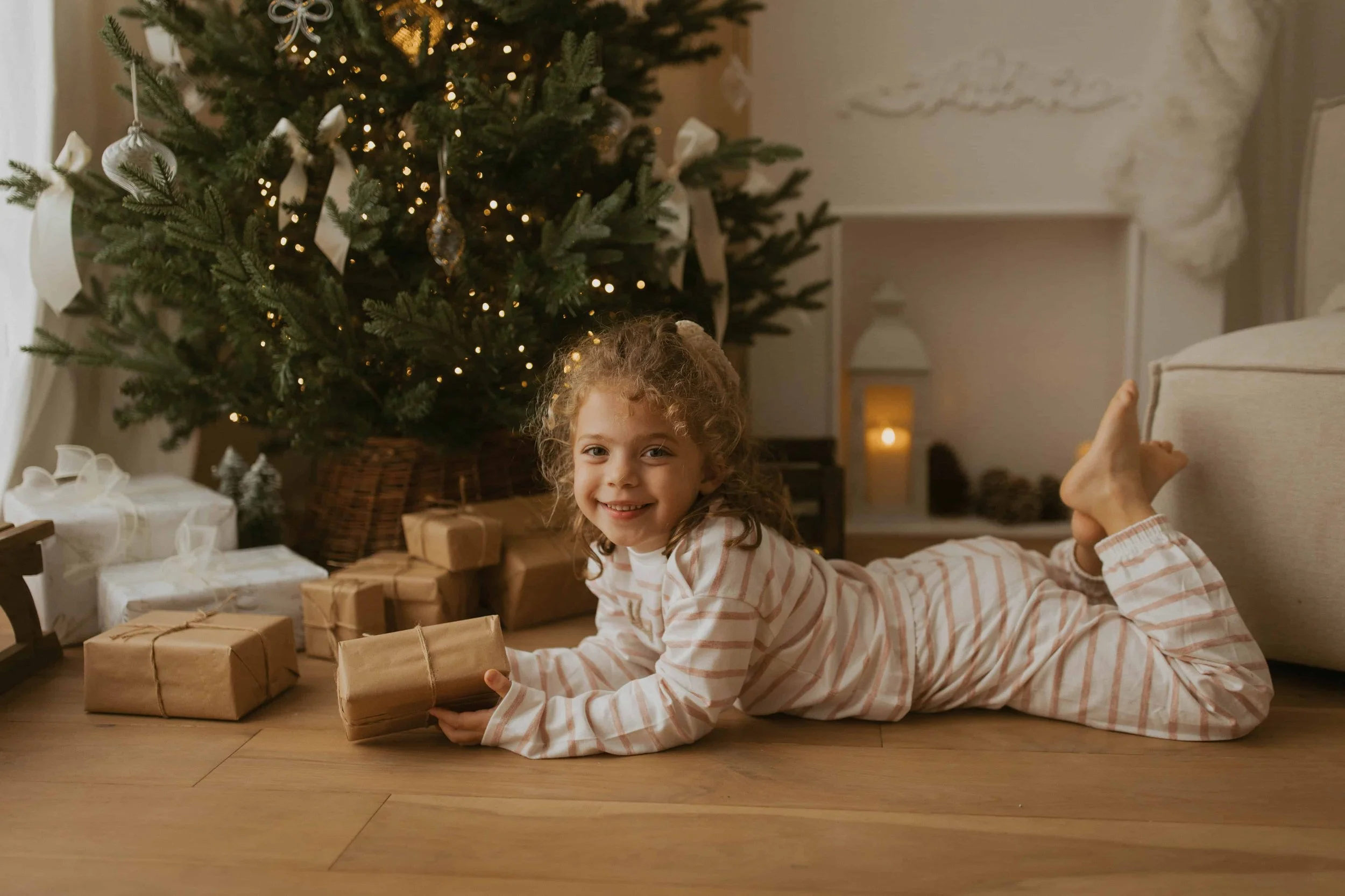 little girl wearing a pyjama from the white company, laying on the floor by a christmas tree in a cosy and warm studio in warlingham surrey