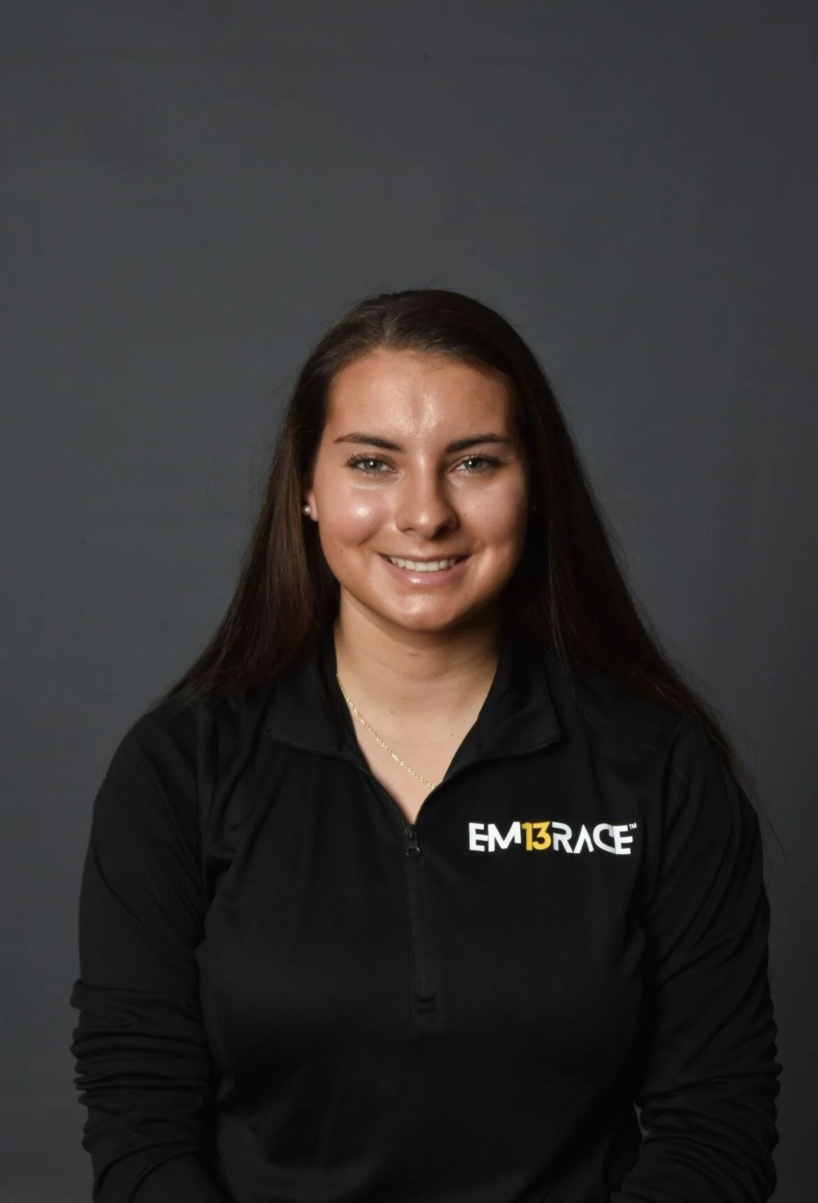 A headshot of Alexia who has long dark hair, wearing a black Em13race sweatshirt.