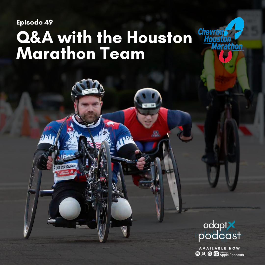 Three men participating in a wheelchair race at the Houston Marathon, with two men in wheelchairs and one cyclist, all wearing helmets and athletic gear, during daytime.
