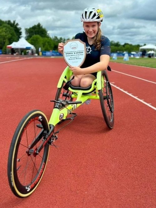 Athlete in a white helmet and navy shirt using a yellow racing wheelchair on a track.