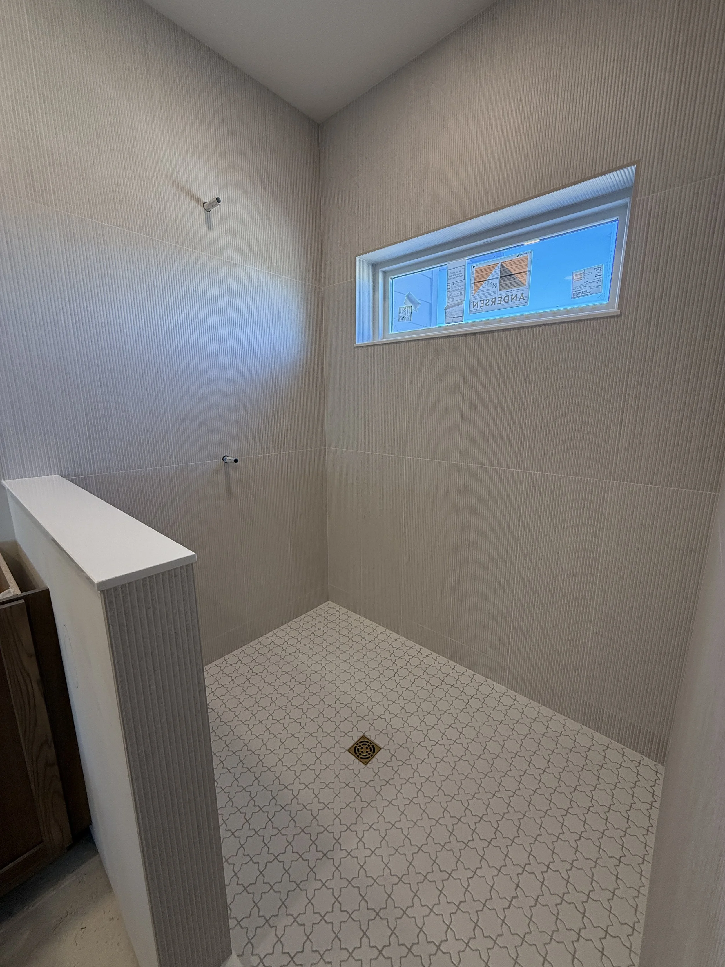Empty shower or bathroom corner with textured walls, patterned tile floor, and a small window.