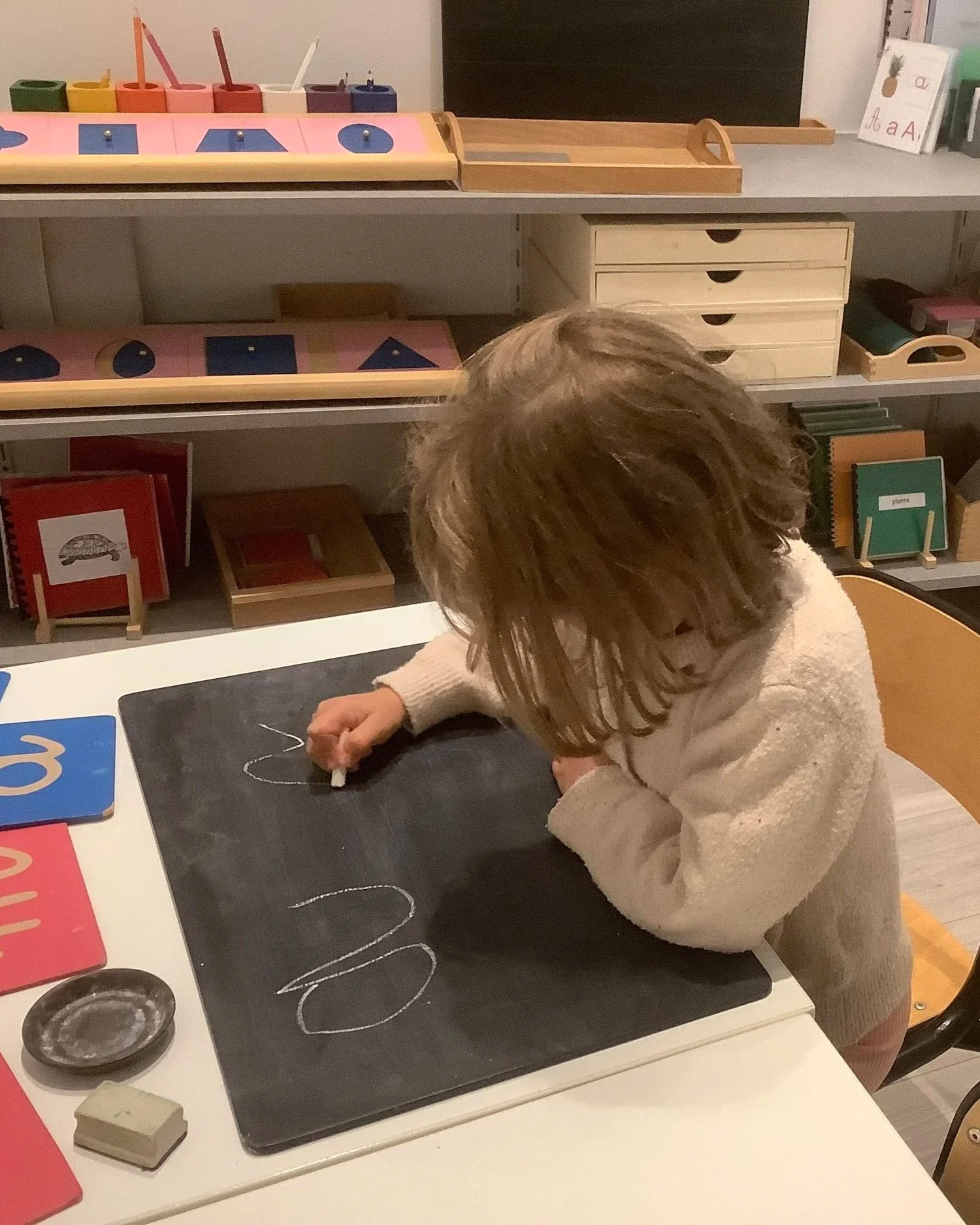 Enfant en maternelle bilingue Montessori qui trace des lettres sur une ardoise pendant un atelier de langage.