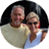Two people standing outdoors, posing for a photo. The person on the left is wearing a black shirt and sunglasses, and the person on the right is wearing glasses and a black dress.