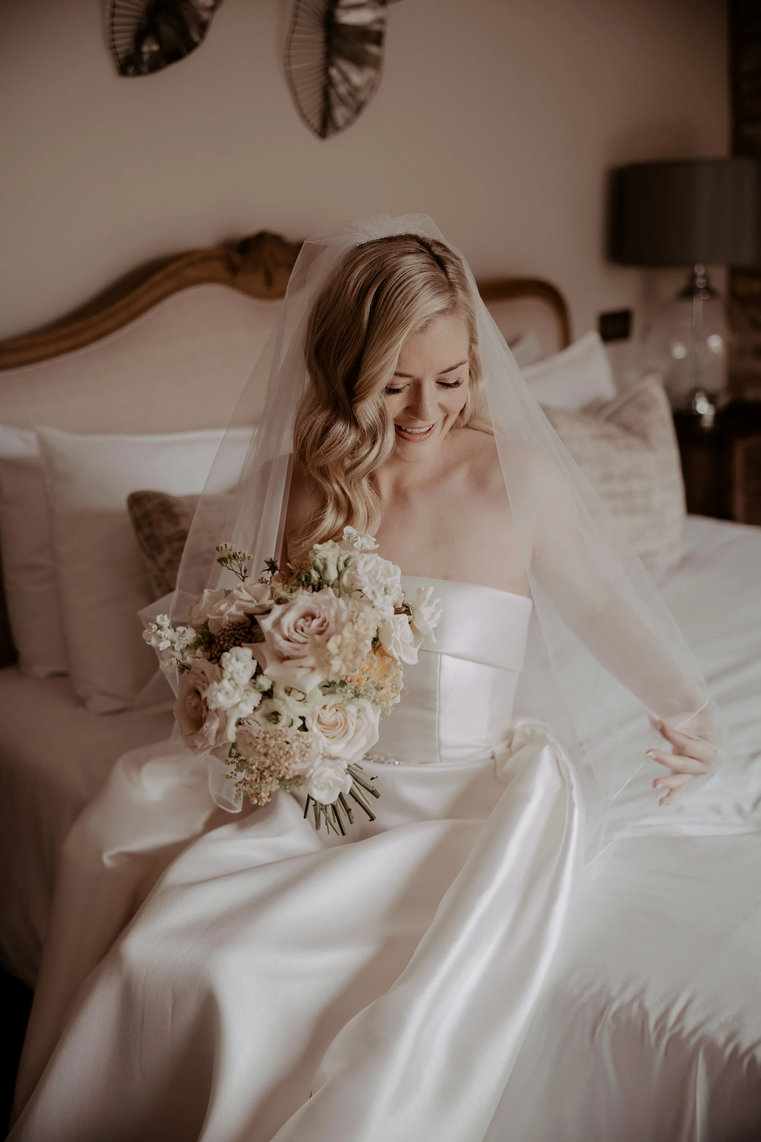 Bride in a white dress and veil holding a blush and cream wedding bouquet.