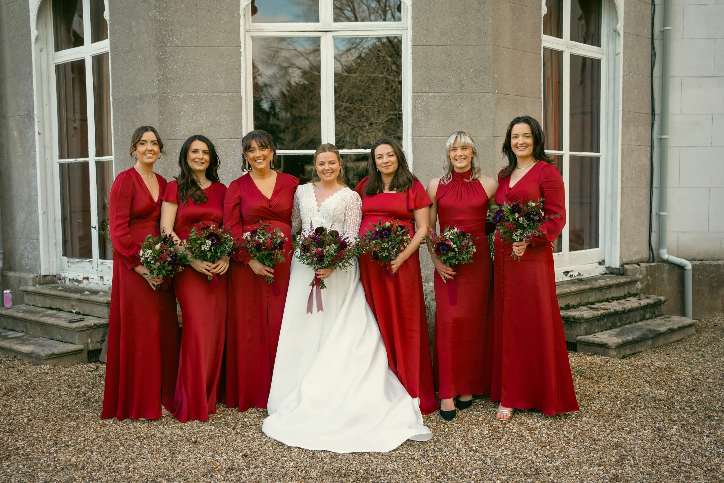 Bride and six bridesmaids in red dresses holding coordinating wedding bouquets.