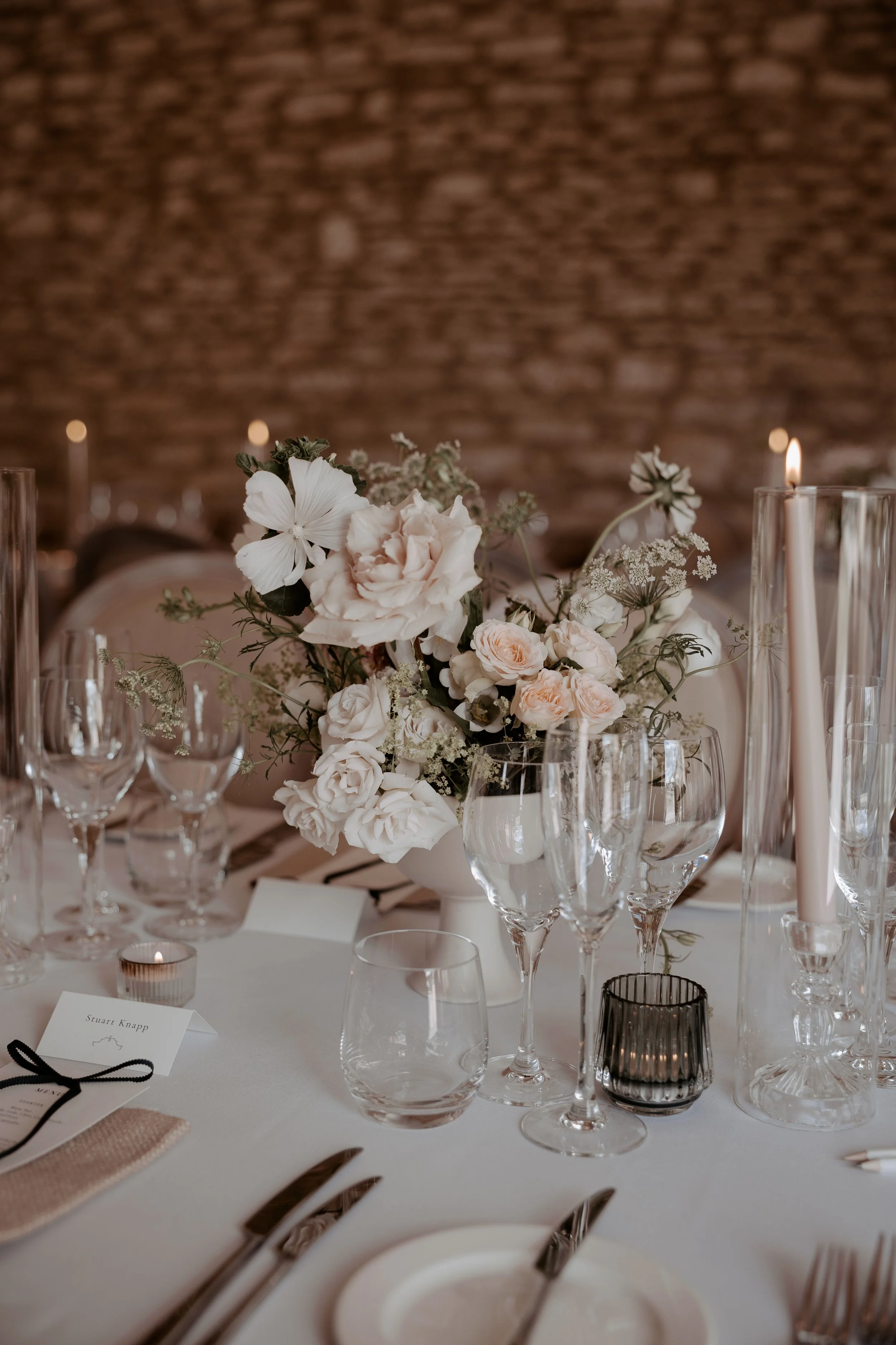 Blush and white wedding table flowers in a footed bowl, surrounded by candles and glassware.