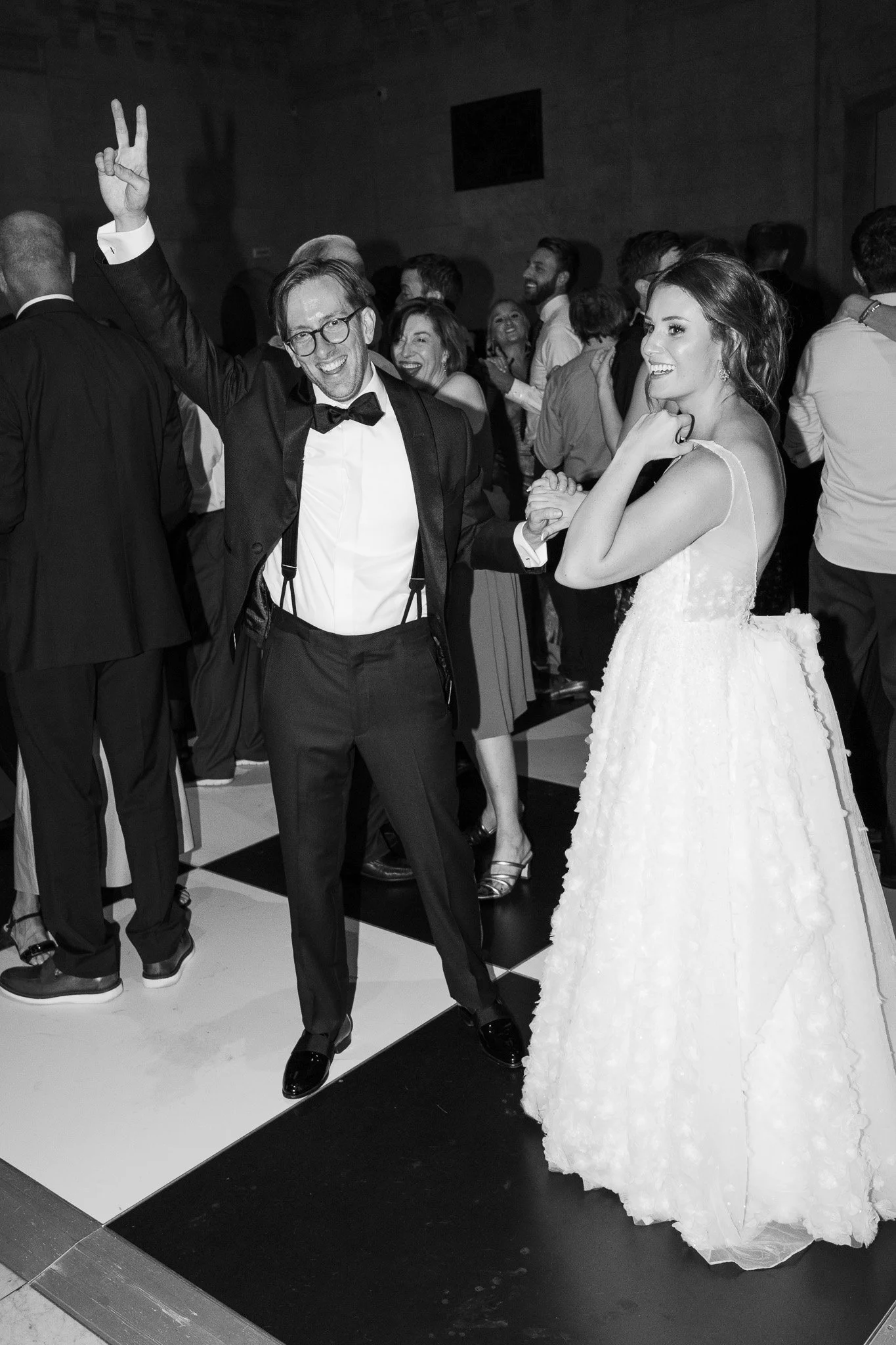 Fine art wedding photography at the cincinnati art museum. People dancing at a wedding reception with a groom in a tuxedo and a bride in a wedding dress, smiling and enjoying the celebration.