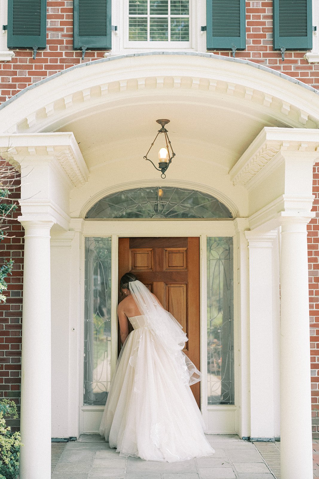Bride in white wedding dress standing at front door of a brick house with columns and glass panels at the French House Cincinnati
