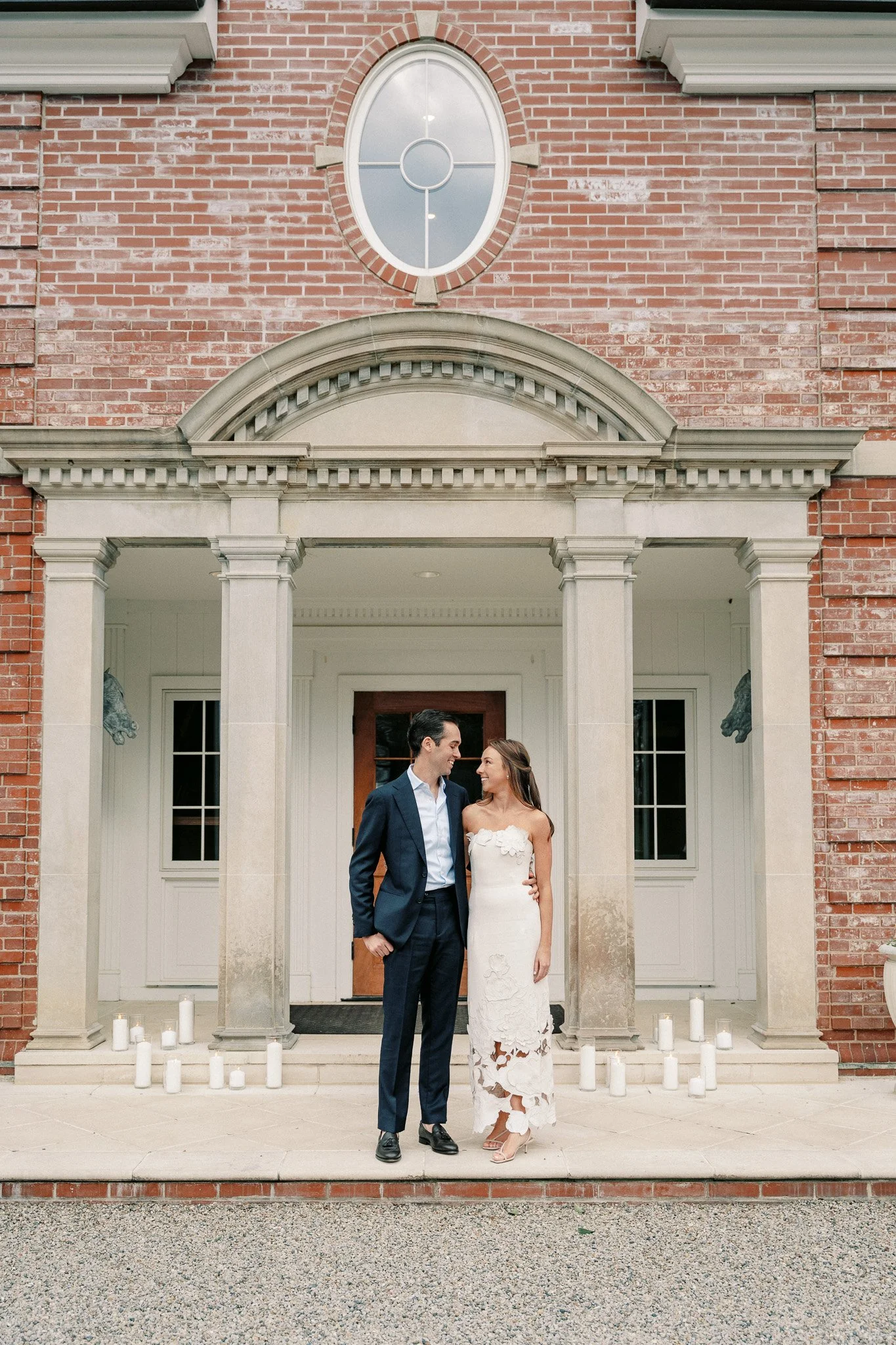 A bride and groom standing arm-in-arm outside a brick building with candles on the steps.