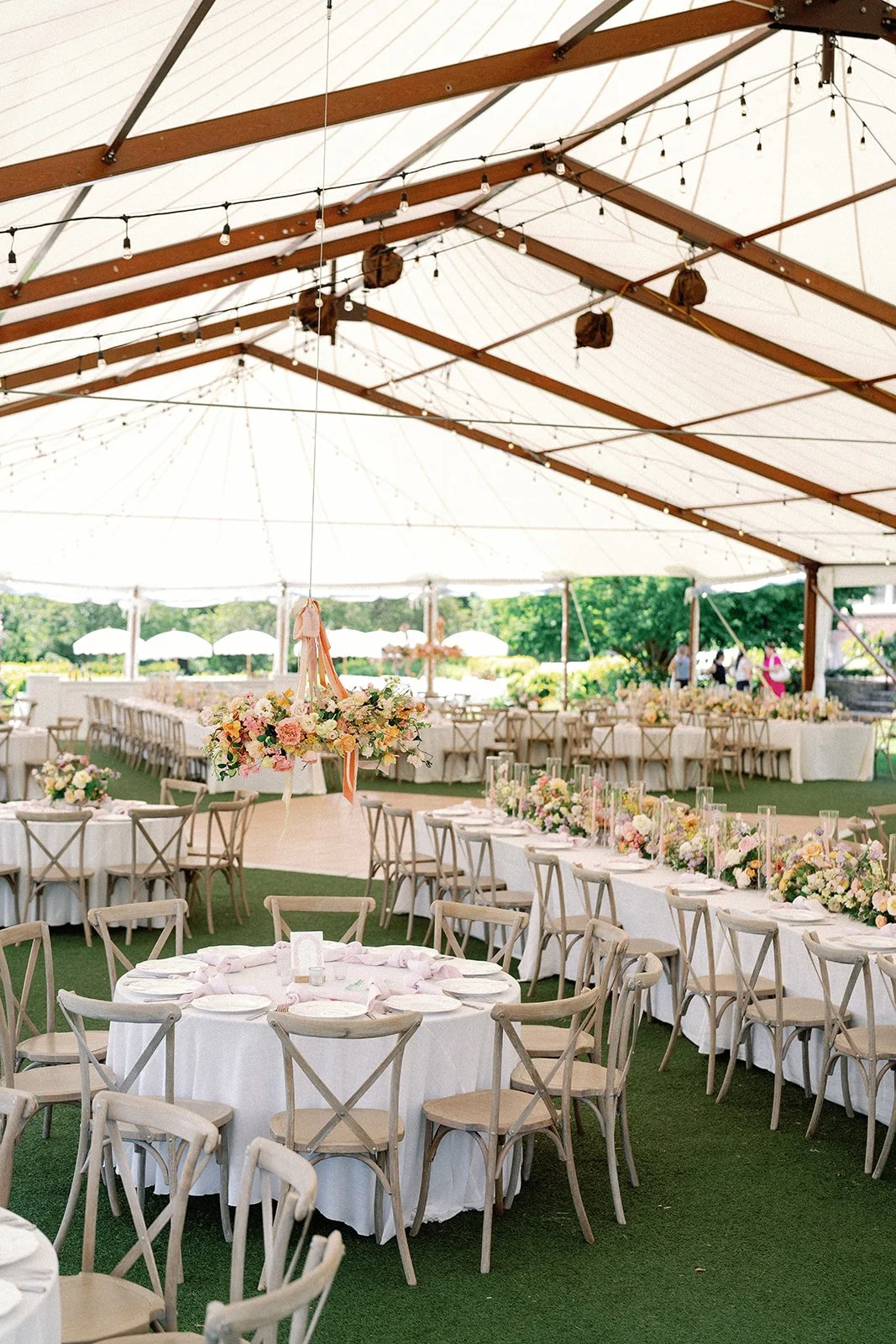 Beautiful outdoor wedding reception under a large white tent with floral arrangements, round and long tables, and wooden chairs. Luxury wedding reception at the French House in Cincinnati