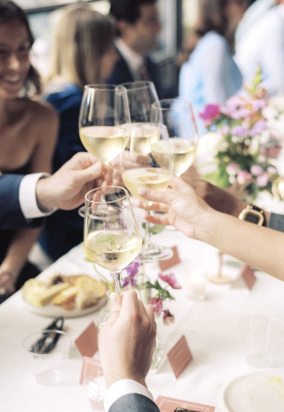 People raising glasses of white wine in a toast at a gathering or celebration.