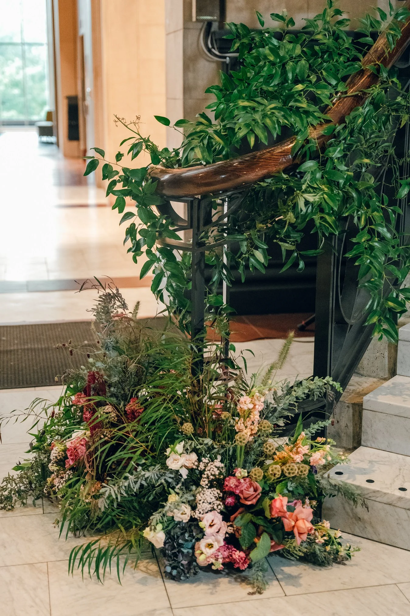 Indoor plant arrangement with green foliage and colorful flowers at the base of a staircase.