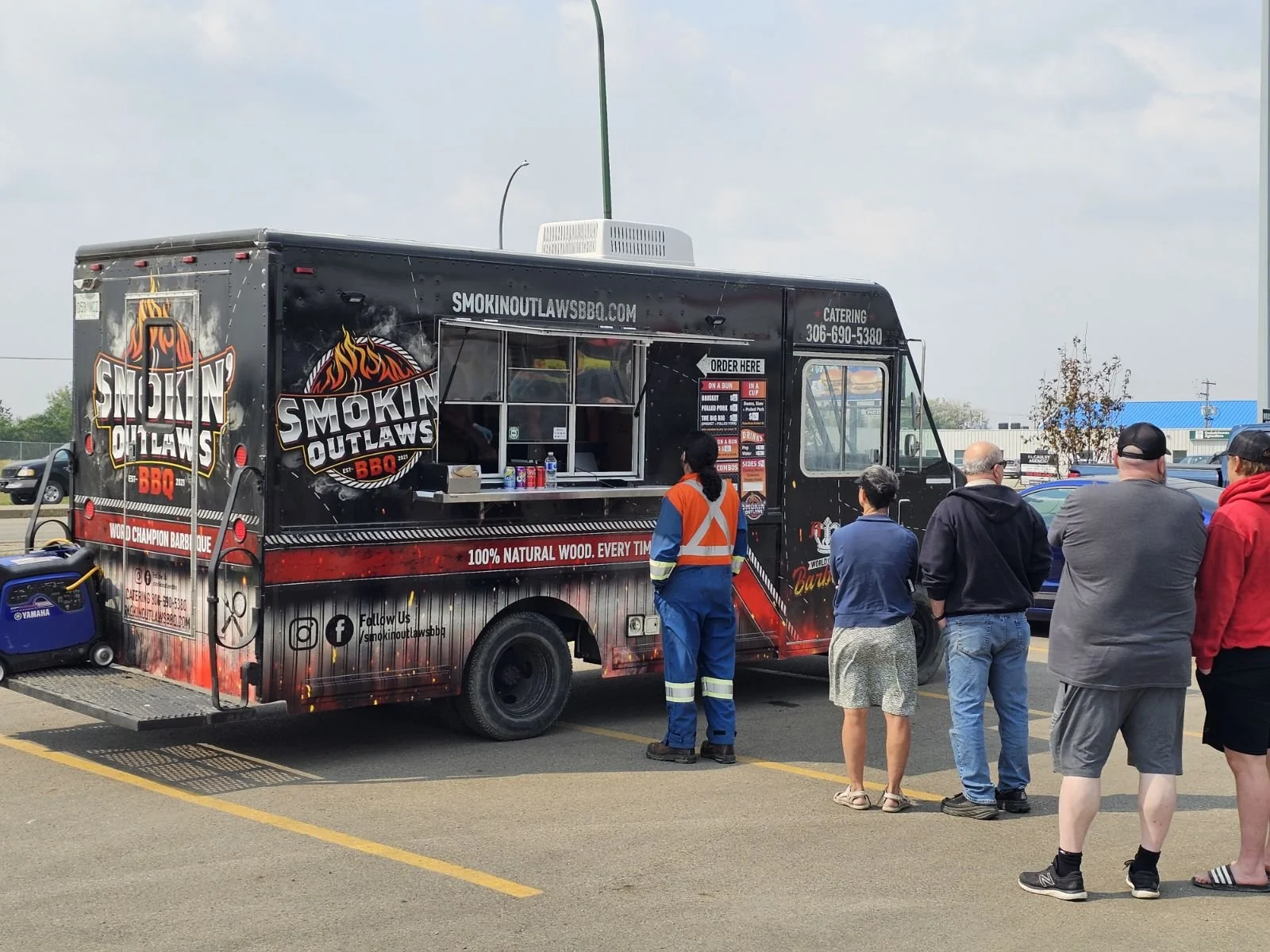 Food truck named Smokin’ Outlaws BBQ parked outdoors with a line of people waiting to order, serving wood champion barbecue.