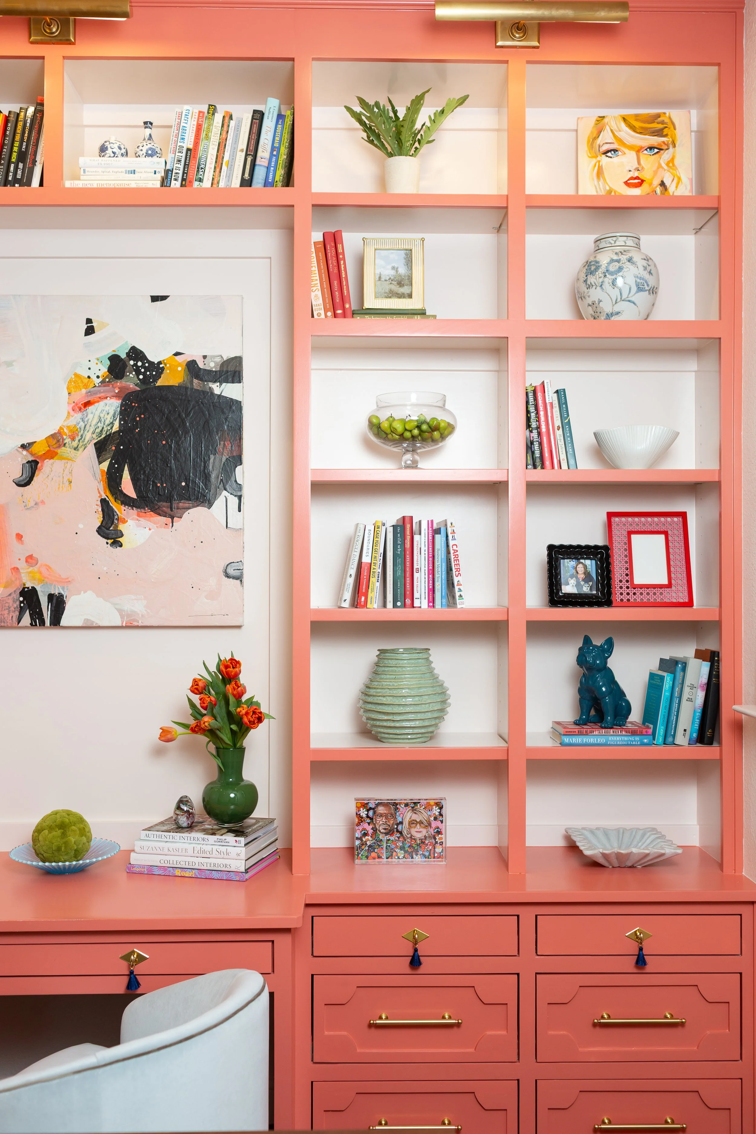 Custom coral built-in home office designed by MASH Habitat Interiors featuring floor-to-ceiling shelving, integrated desk, custom cabinetry, brass hardware, library lighting, and styled decorative accessories in a Fort Worth luxury home.