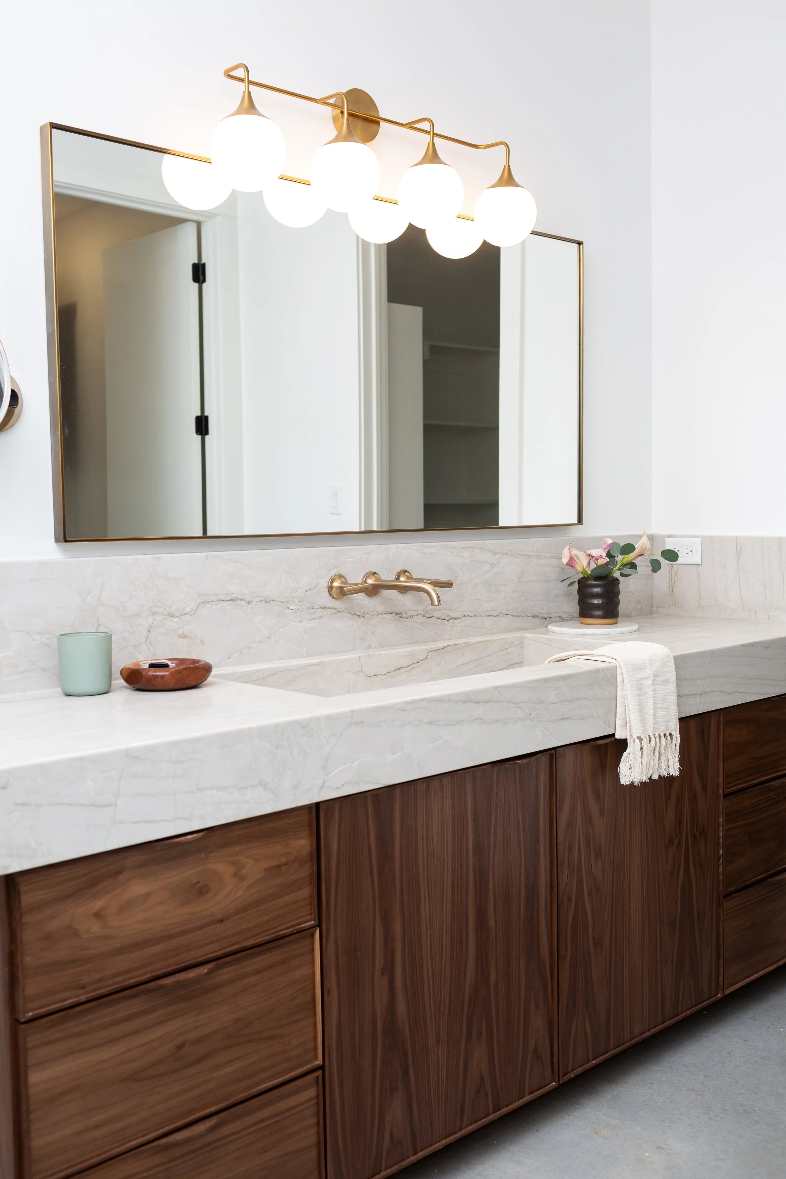Custom walnut vanity with integrated stone sink, brass faucet, and contemporary globe vanity lighting in a modern luxury bathroom remodel.