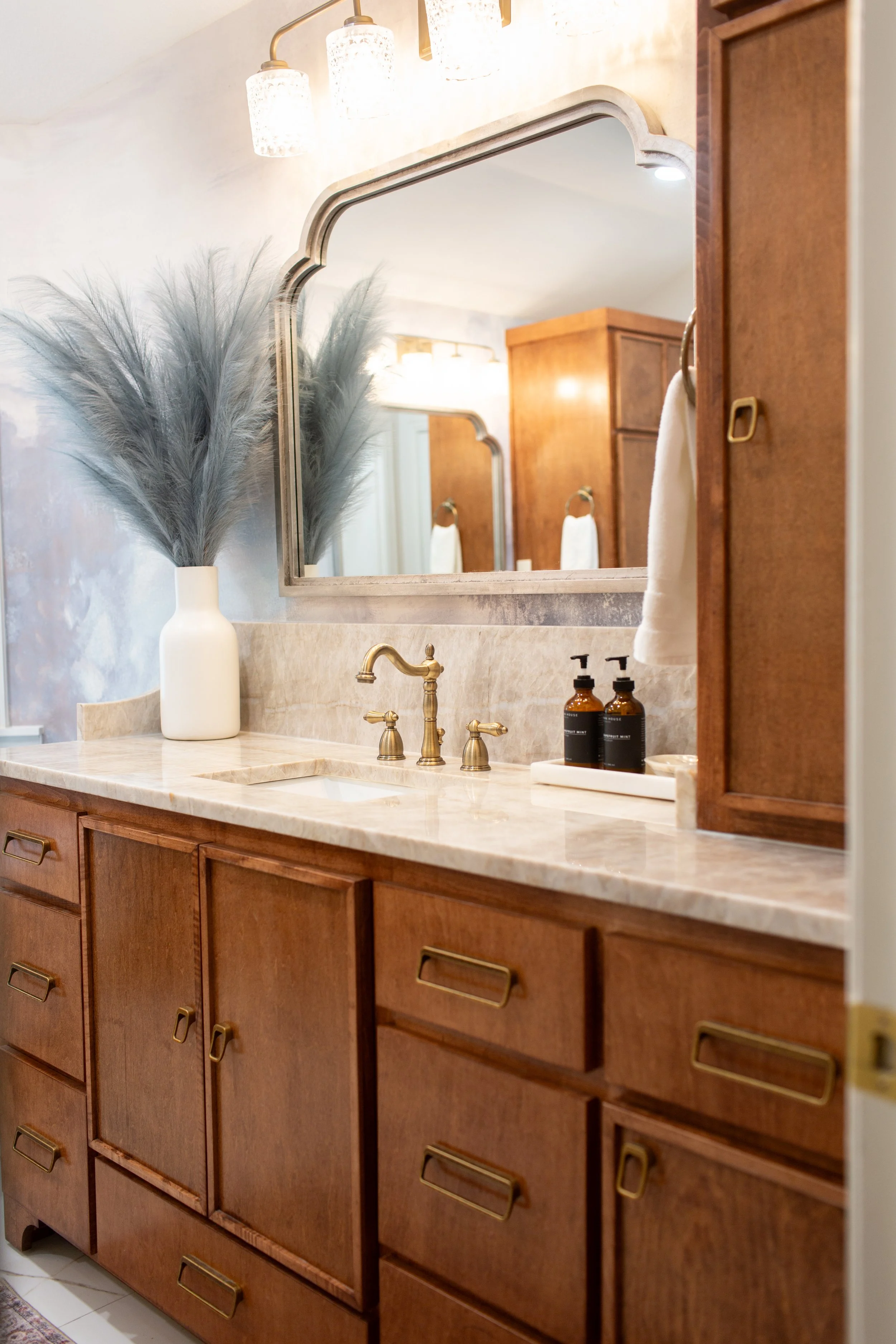 Warm wood bathroom vanity with marble countertops, aged brass fixtures, and organic accessories designed by MASH Habitat Interiors.