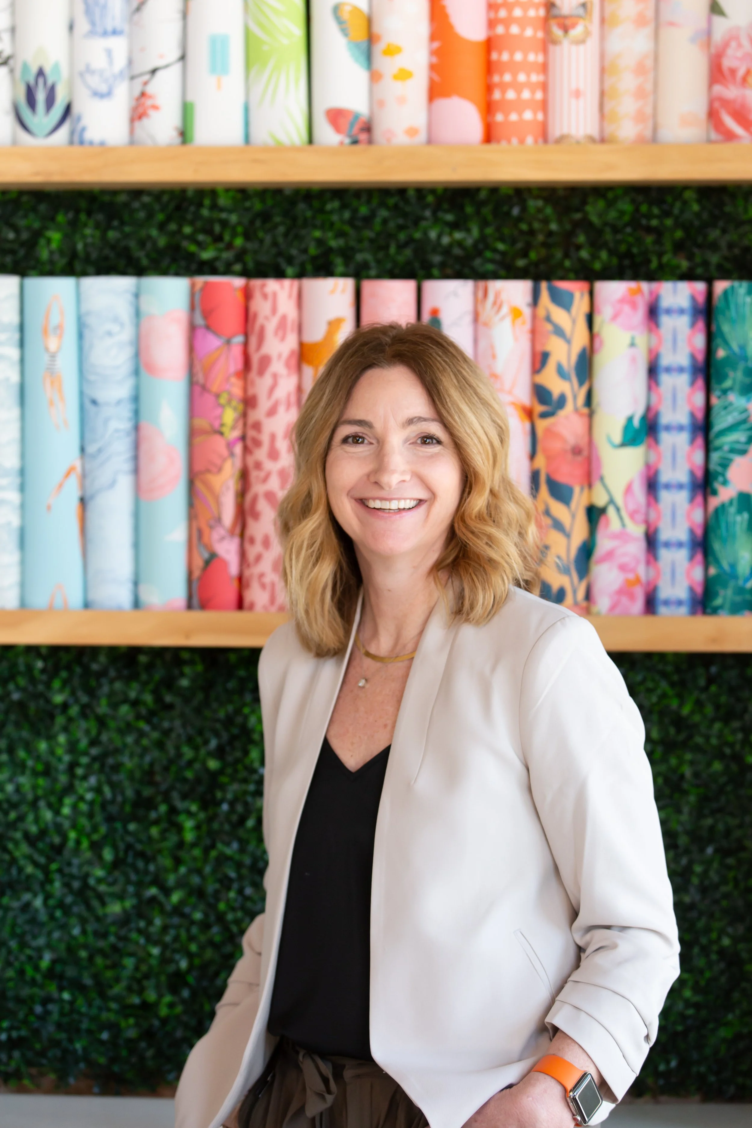 Interior designer standing in front of a colorful wallpaper library at MASH Habitat Interiors design studio in Fort Worth.