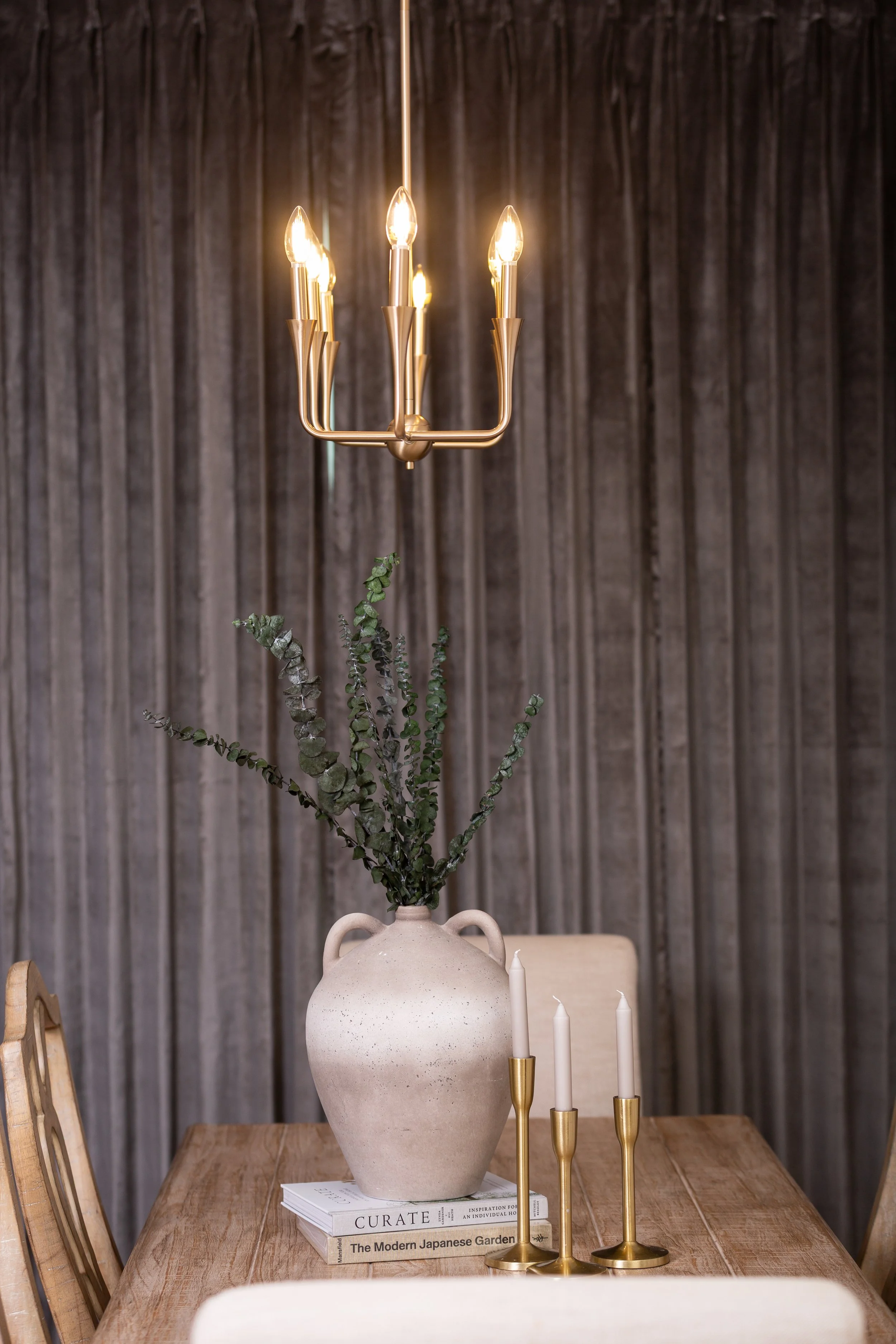 Styled dining room featuring a brass chandelier, textured wall treatment, and natural ceramic vase by MASH Habitat Interiors