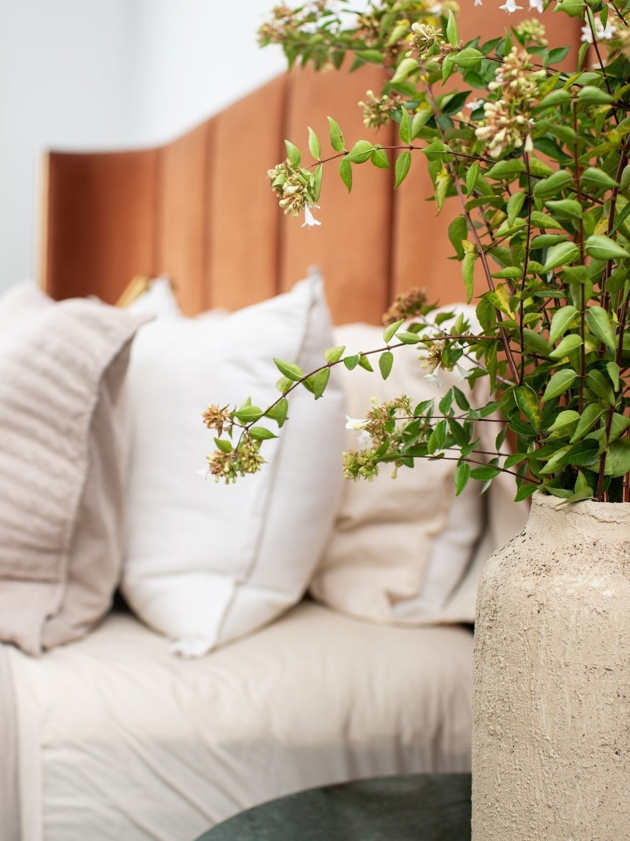 Bedroom styling with layered neutral bedding, warm wood accents, and fresh greenery creating a peaceful retreat.