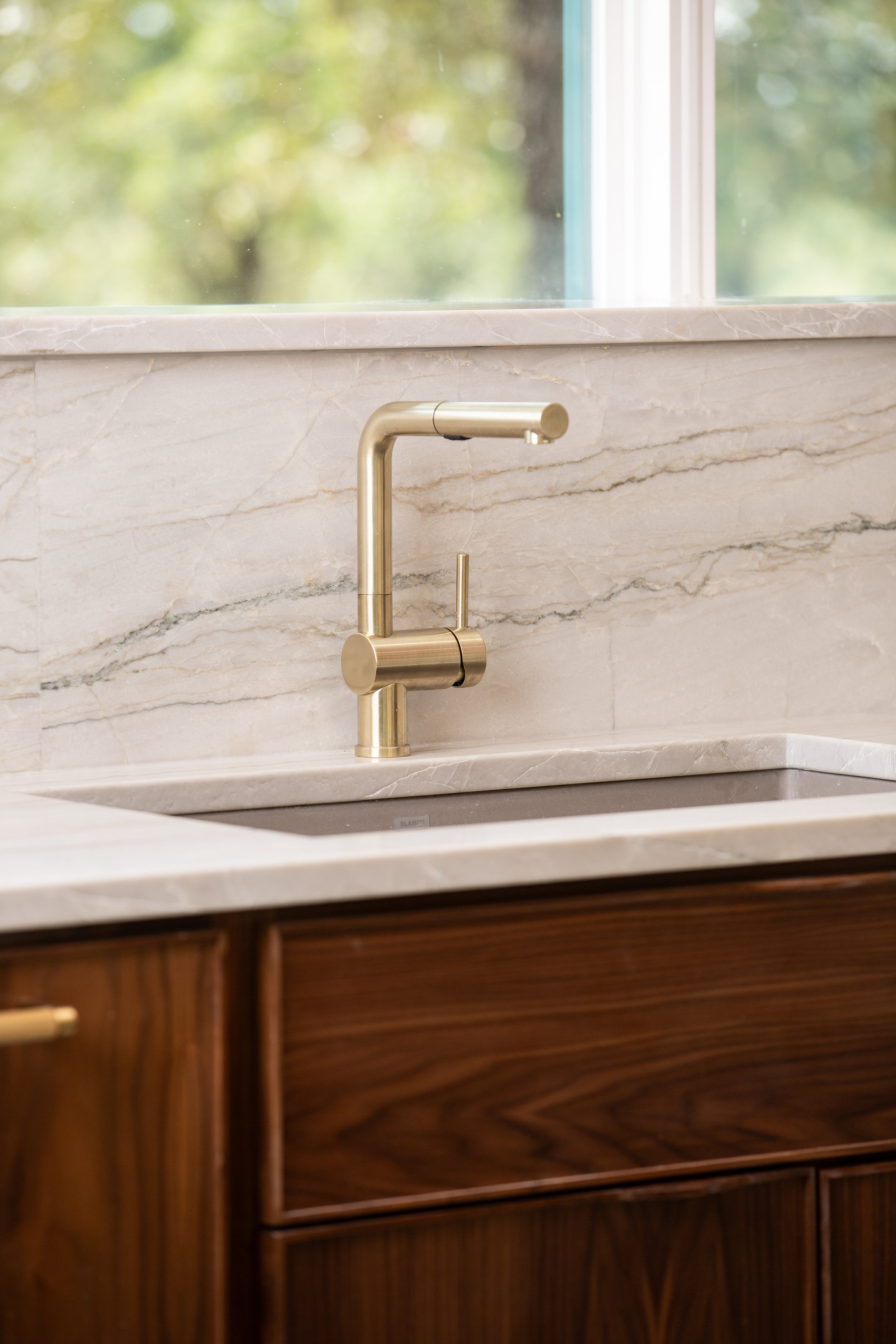 Luxury kitchen with walnut cabinets, natural stone backsplash, and brushed brass faucet.