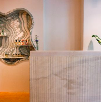 Part of a beige upholstered headboard and a decorative wall mirror with a swirling pattern in a bedroom.