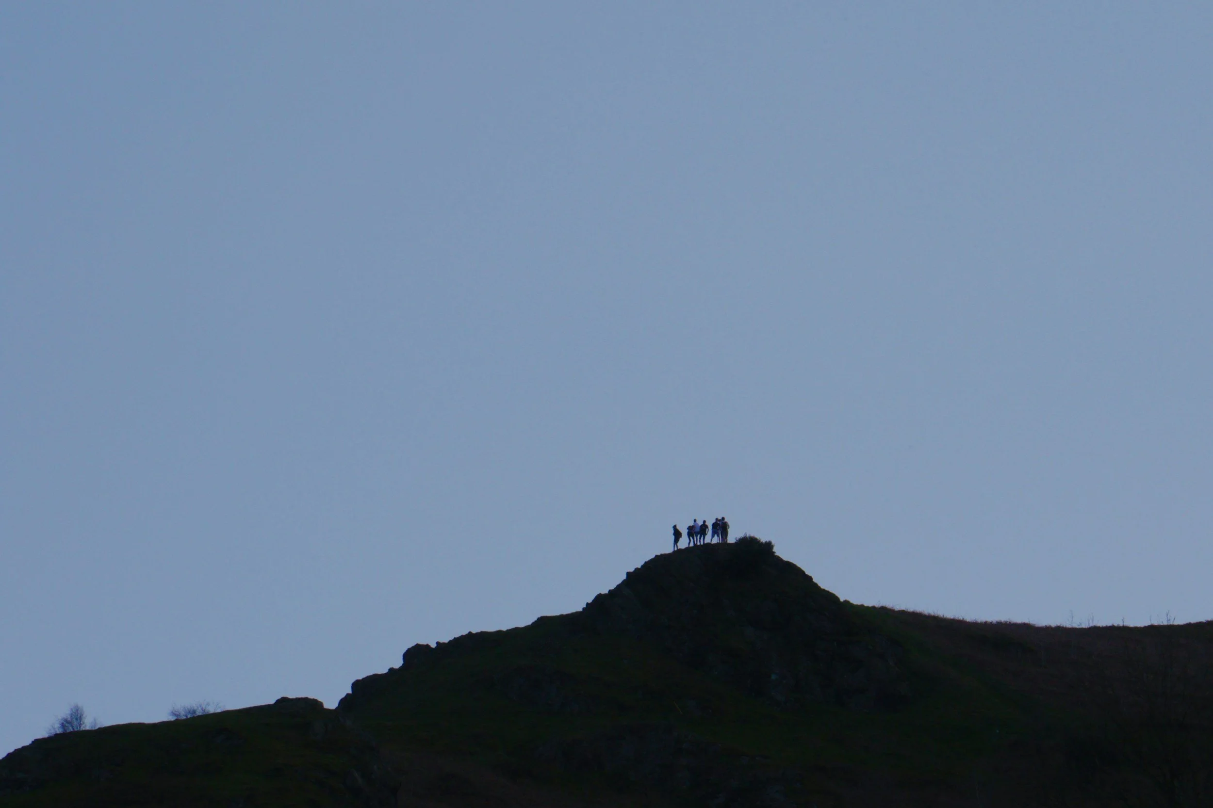 Group of people standing on a mountain peak during dusk or dawn.