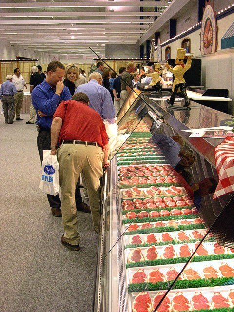 Tyler sales and subject-matter experts talk with customers and dealers while walking the Tyler showroom where showcases merchandised with faux foods and packaging is accompanied with visual displays.