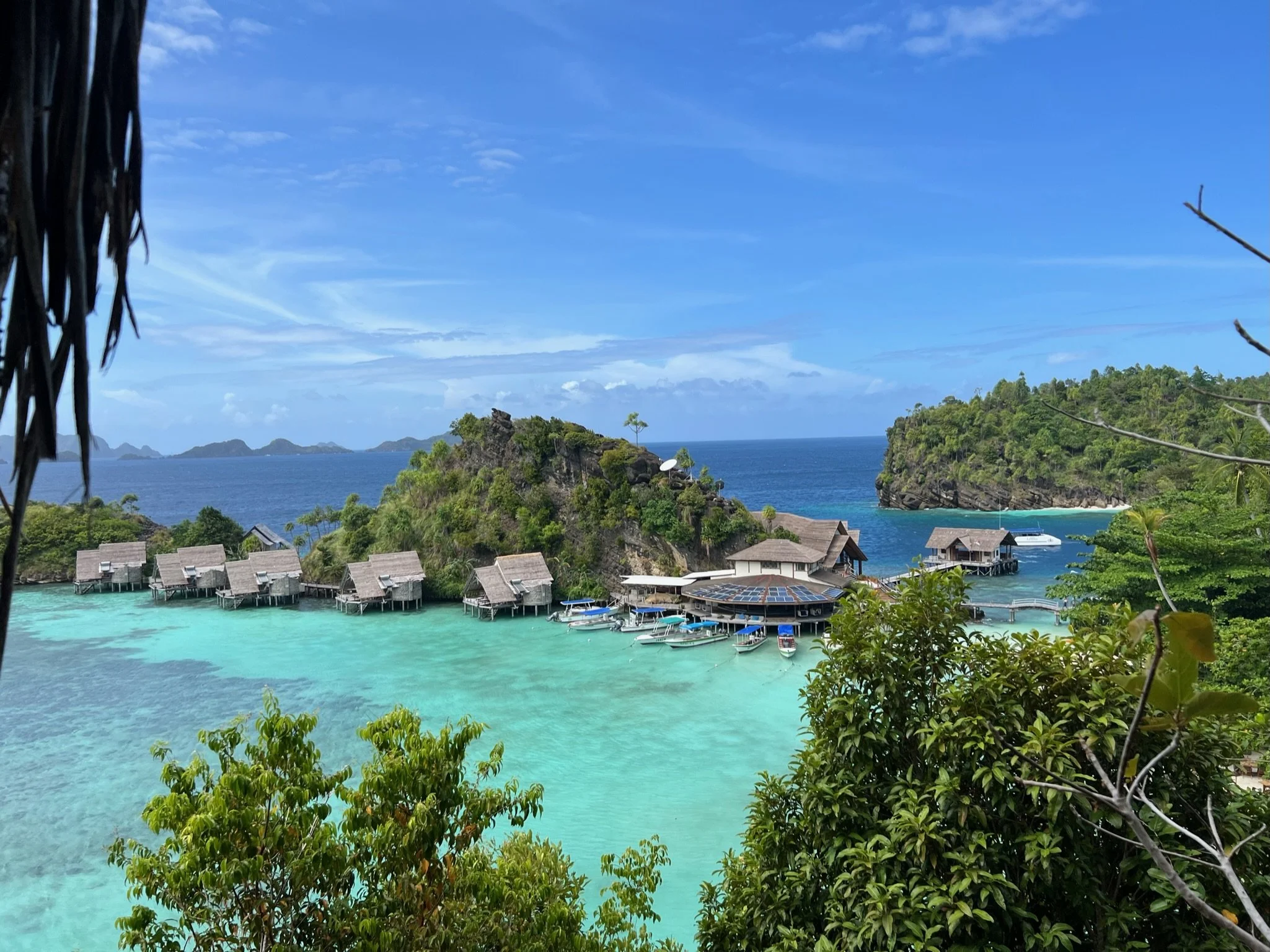 Tropical island scene with turquoise water, overwater bungalows, and lush green hills under a blue sky.