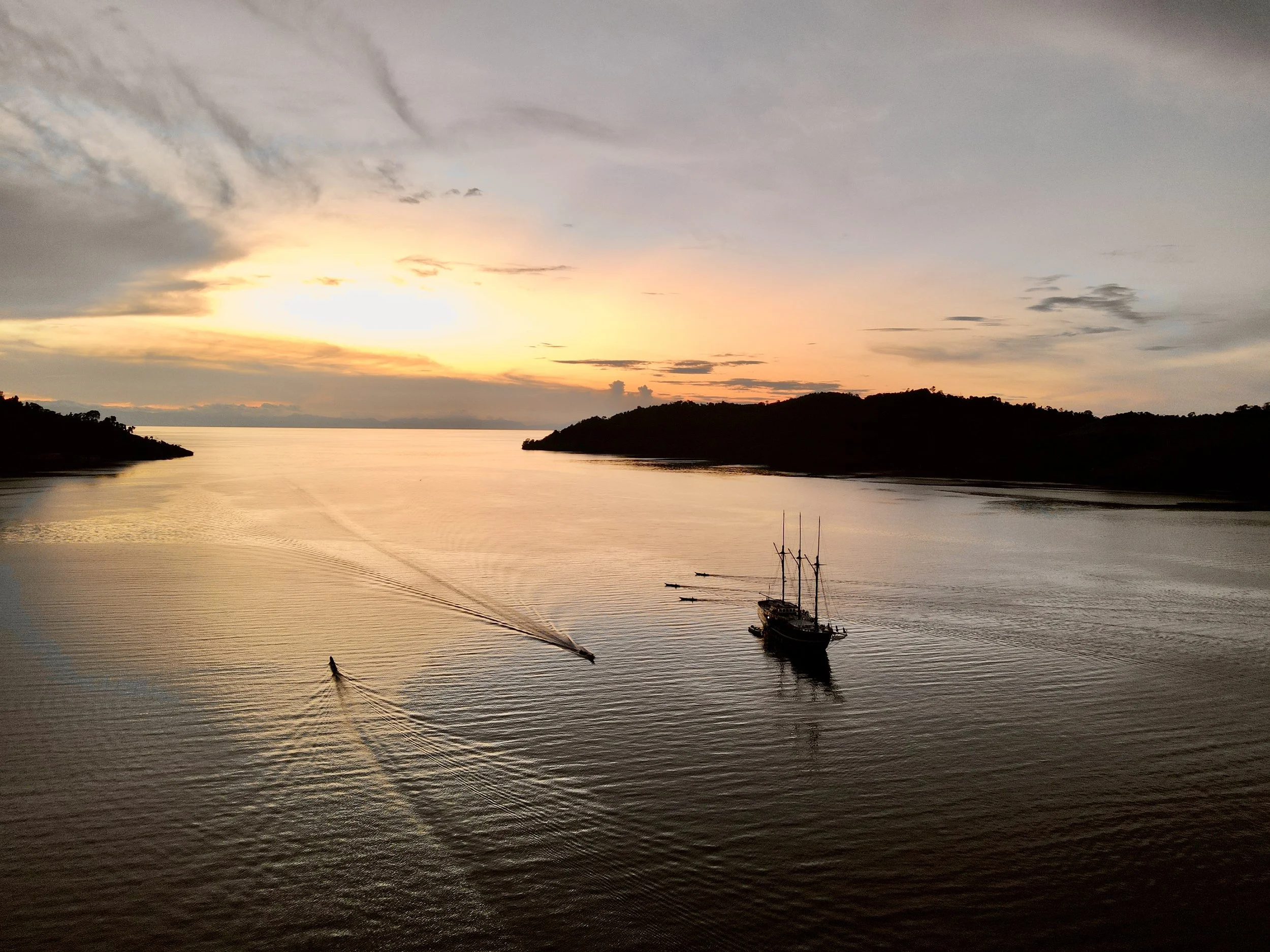 Boat sailing on a calm river during sunset with hills on each side and a partly cloudy sky.