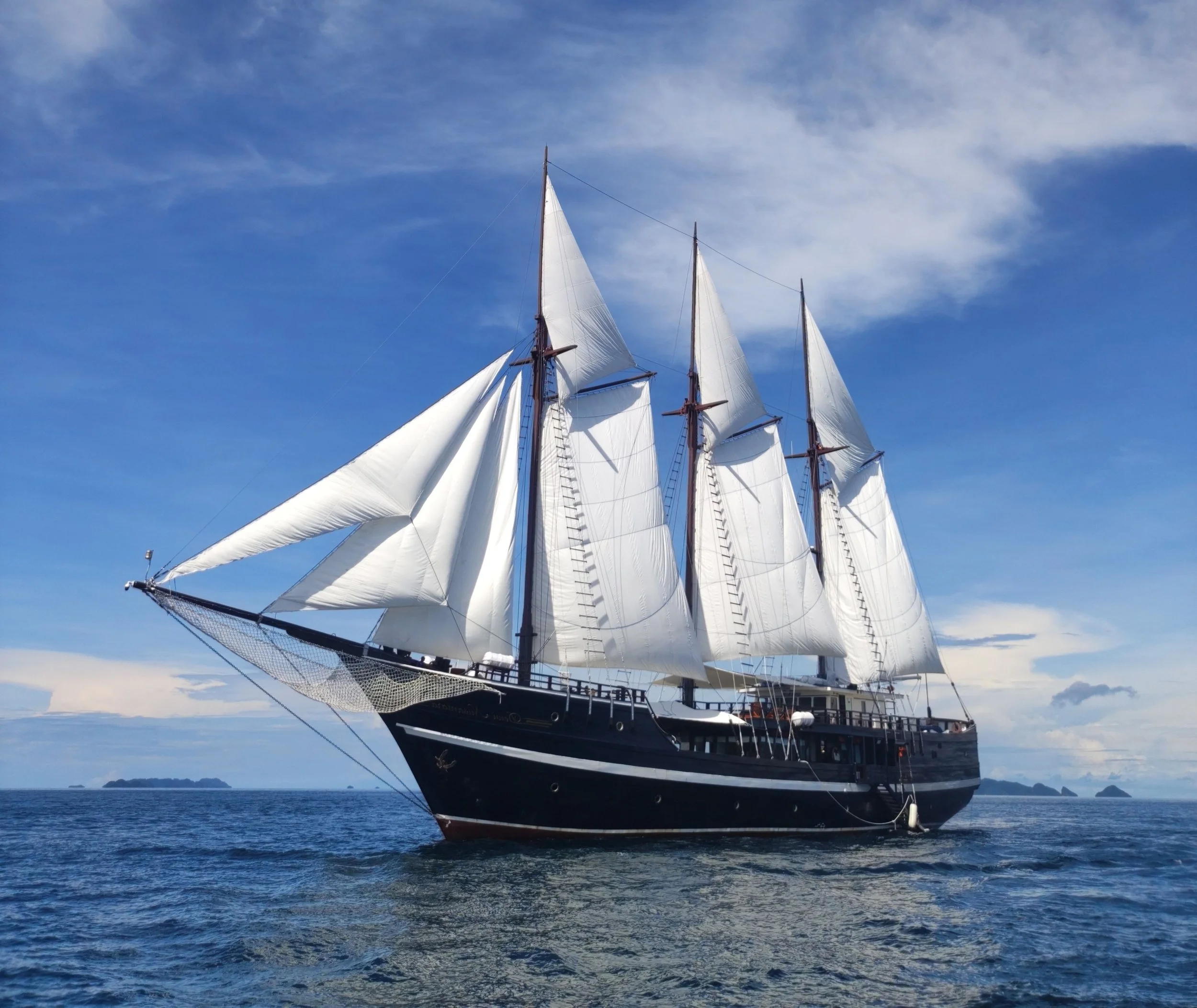 A large sailing ship with white sails on the ocean under a blue sky with some clouds.