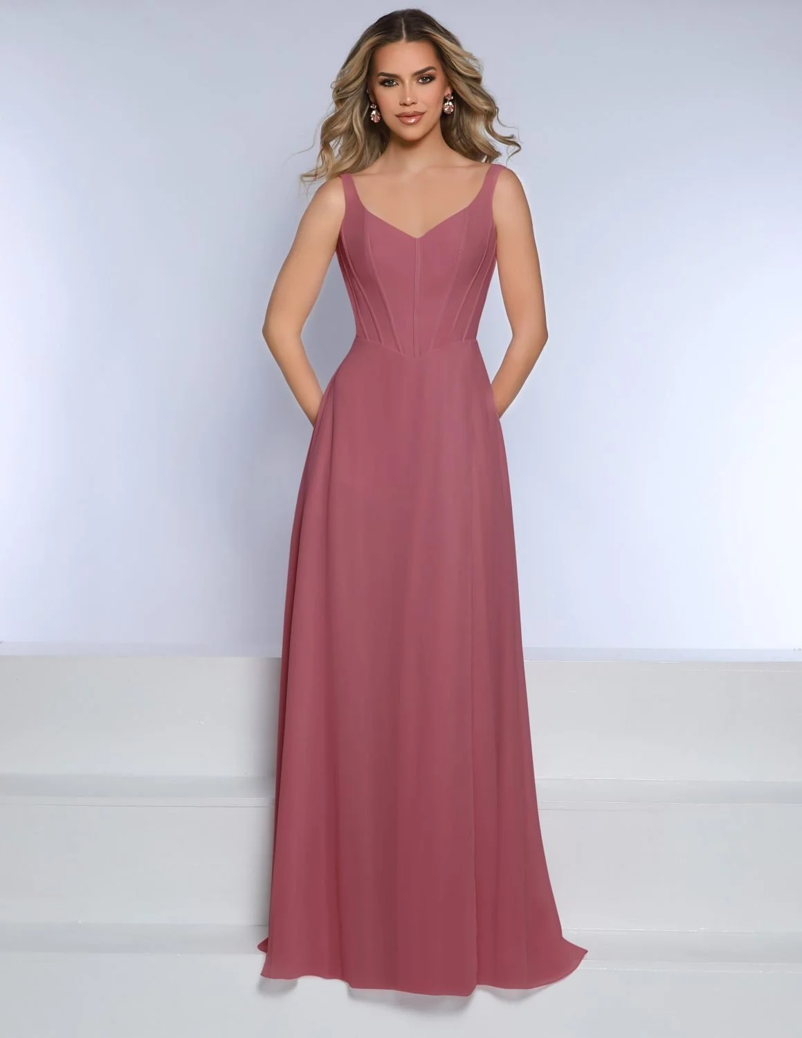 Woman wearing a long, sleeveless, pink gown with fitted bodice, standing against a plain background.