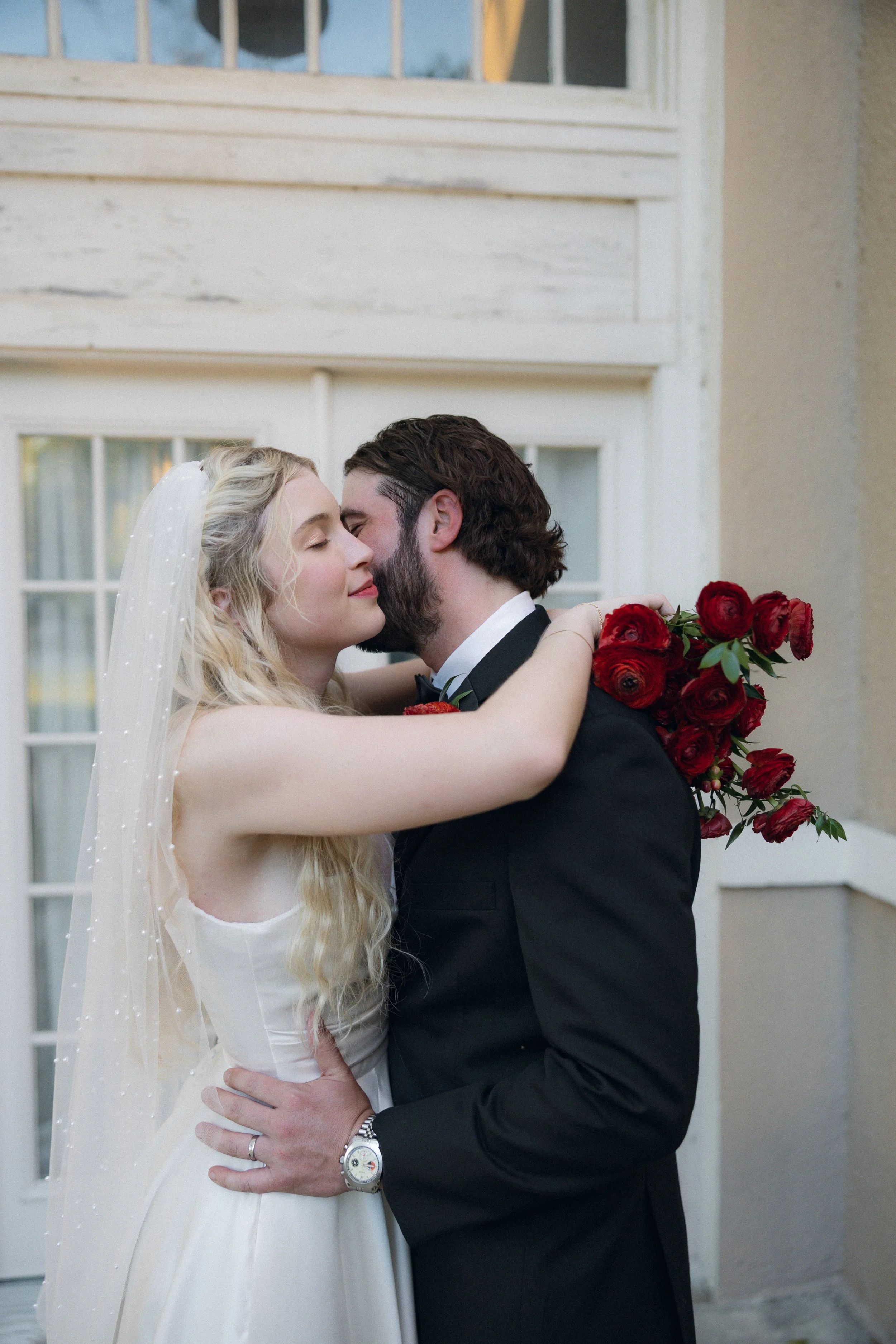 Bride and groom sharing a romantic embrace, bride holding a bouquet of red roses.