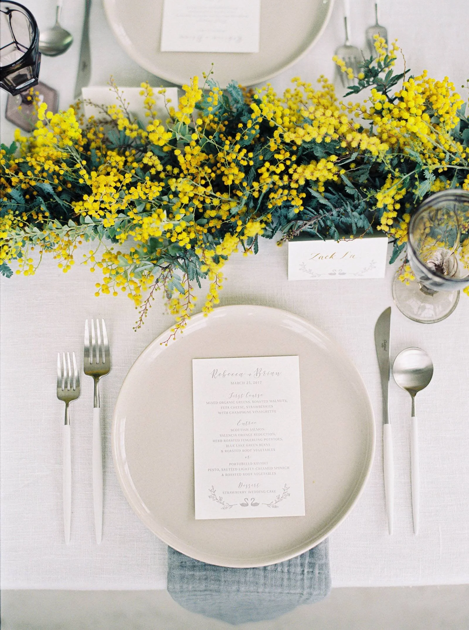 A wedding table scape in warm neutrals is accented by a garland of bright yellow mimosa flower