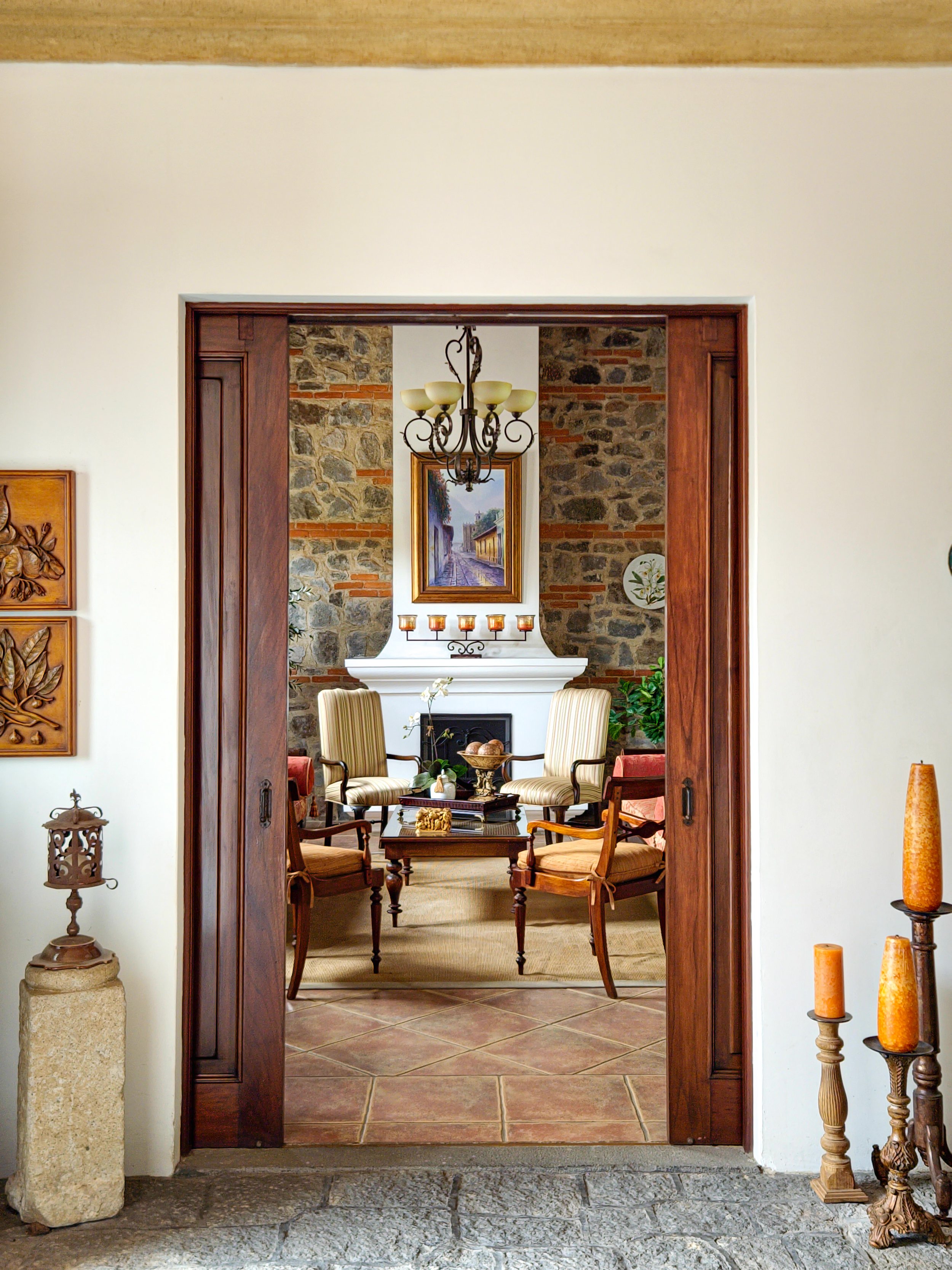 Un pequeño patio con plantas verdes, una mesa blanca con una maceta de plantas altas y una silla, al fondo una pared gris y ventanas con cortinas blancas.