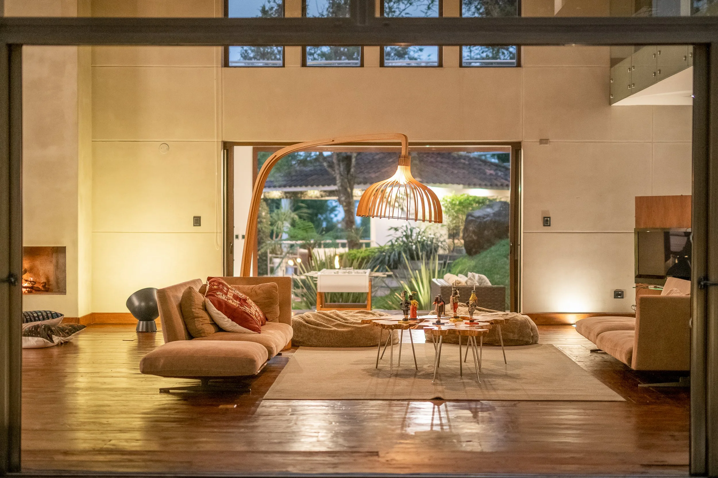 Sala de estar con muebles modernos, lámpara de madera, ventanas grandes y vista a un jardín